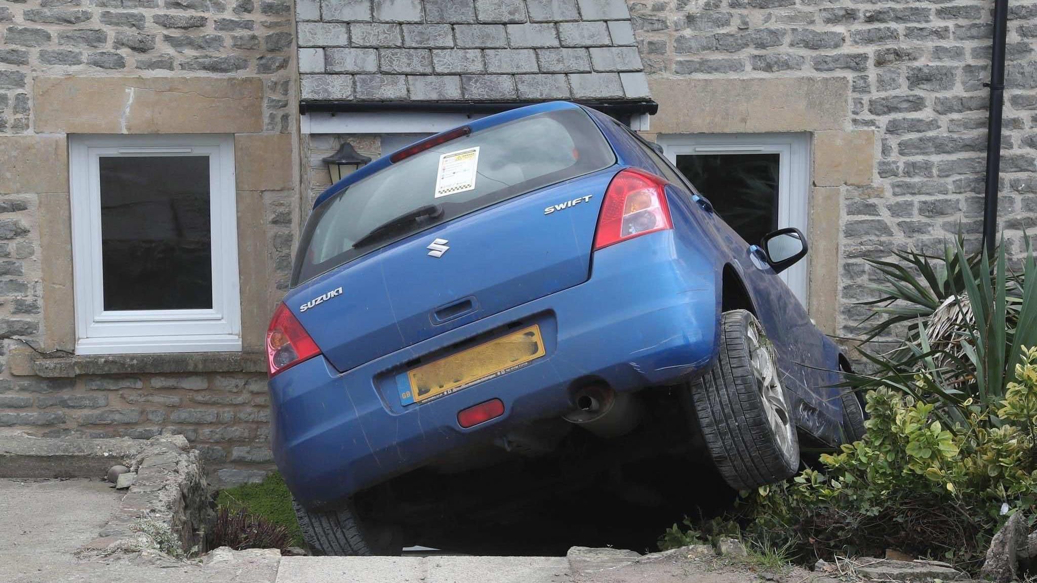 A blue Suzuki Swift crashes into the steps leading to a house.