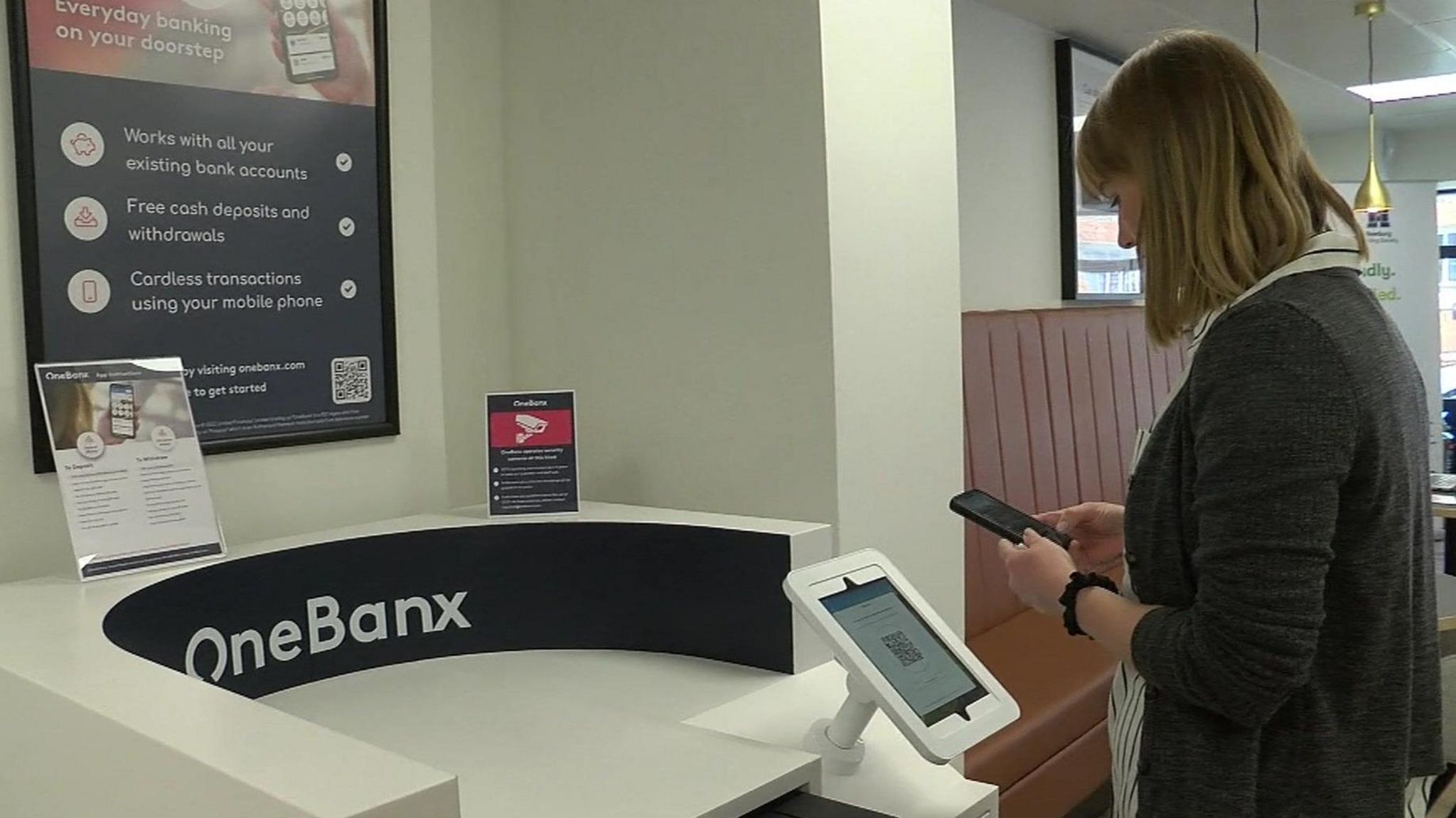 Female customer with phone stands by white banking hub desk