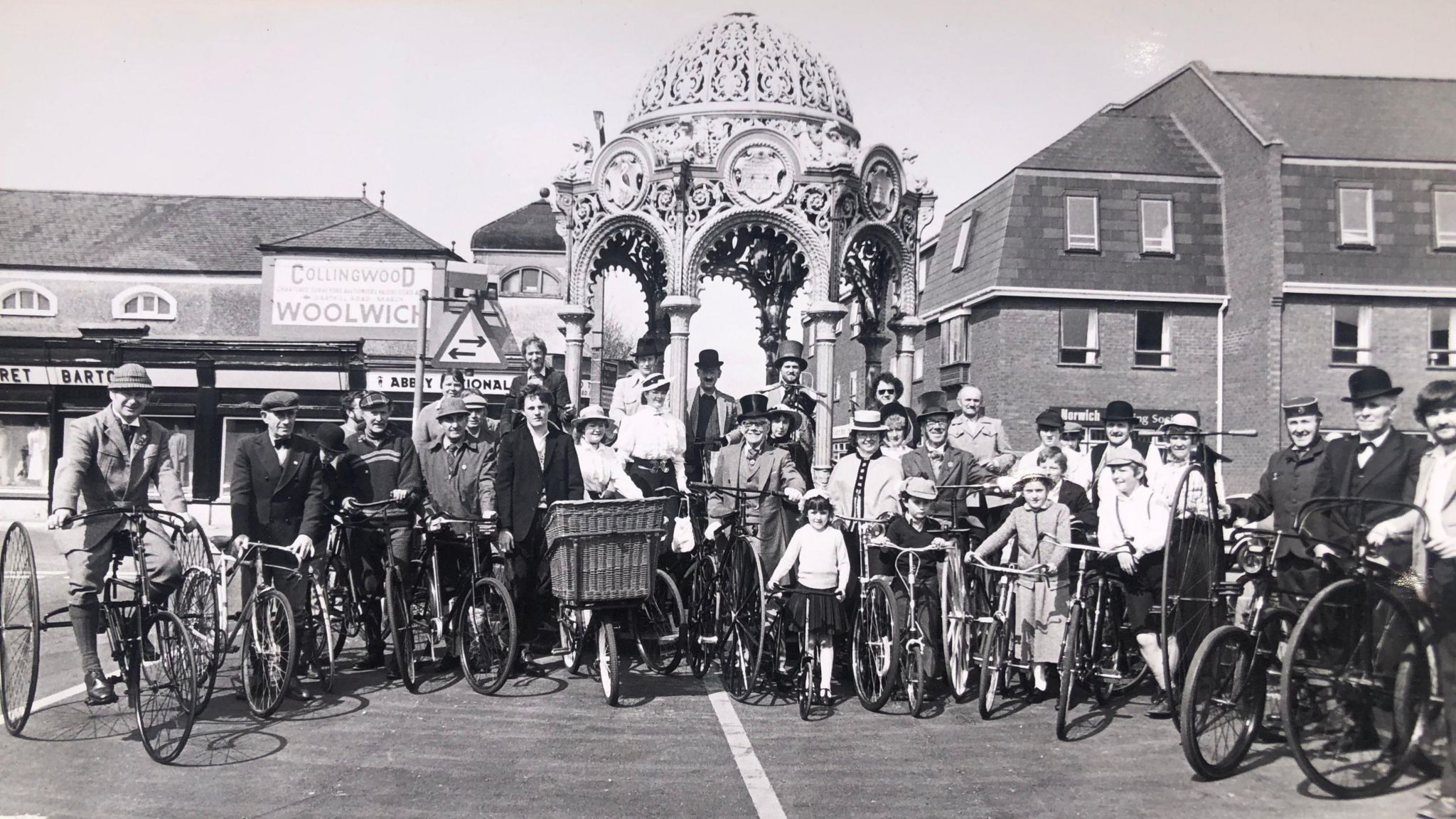 A black and white image of a row of people on vintage bikes dressed in vintage costumes