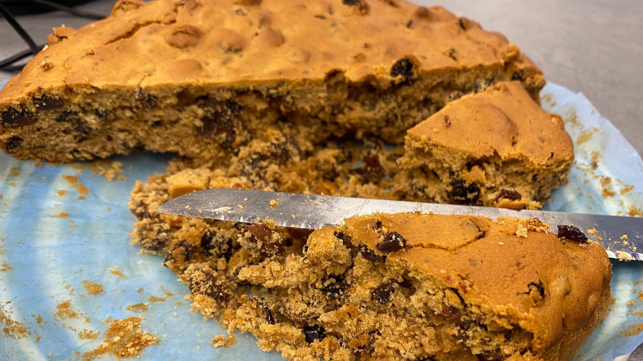 A half-eaten cake on a plate with a large slice cut off and a knife lying across it