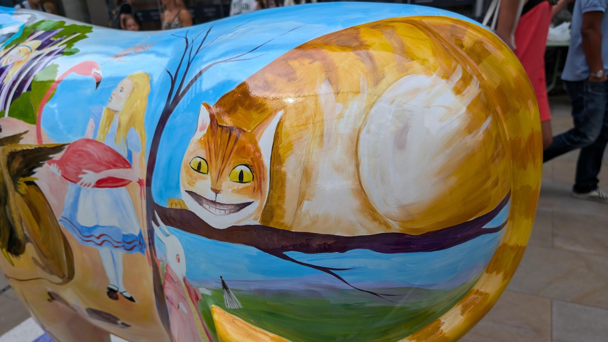 An illustration of Alice on Wonderland is painted on to the life size sculpture of an Ox as part of a charity fundraising art trail around Oxford. A grinning image of the Cheshire Cat, the white rabbit and Alice holding a flamingo are seen.