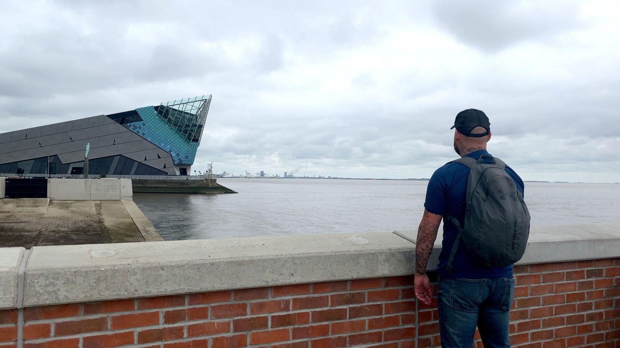 John Levesley, with his back to the camera, standing by a wall looks out over the murky Humber estuary. 