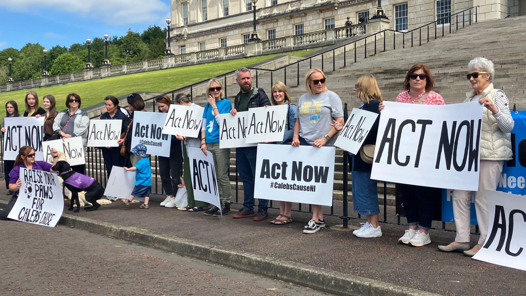 Protestors outside of Stormont holding signs that say 'Act Now'
