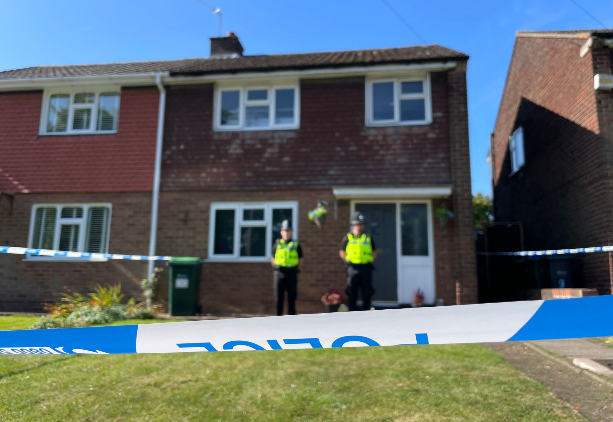 Police officers in uniform stand in front of a house cordoned off by police