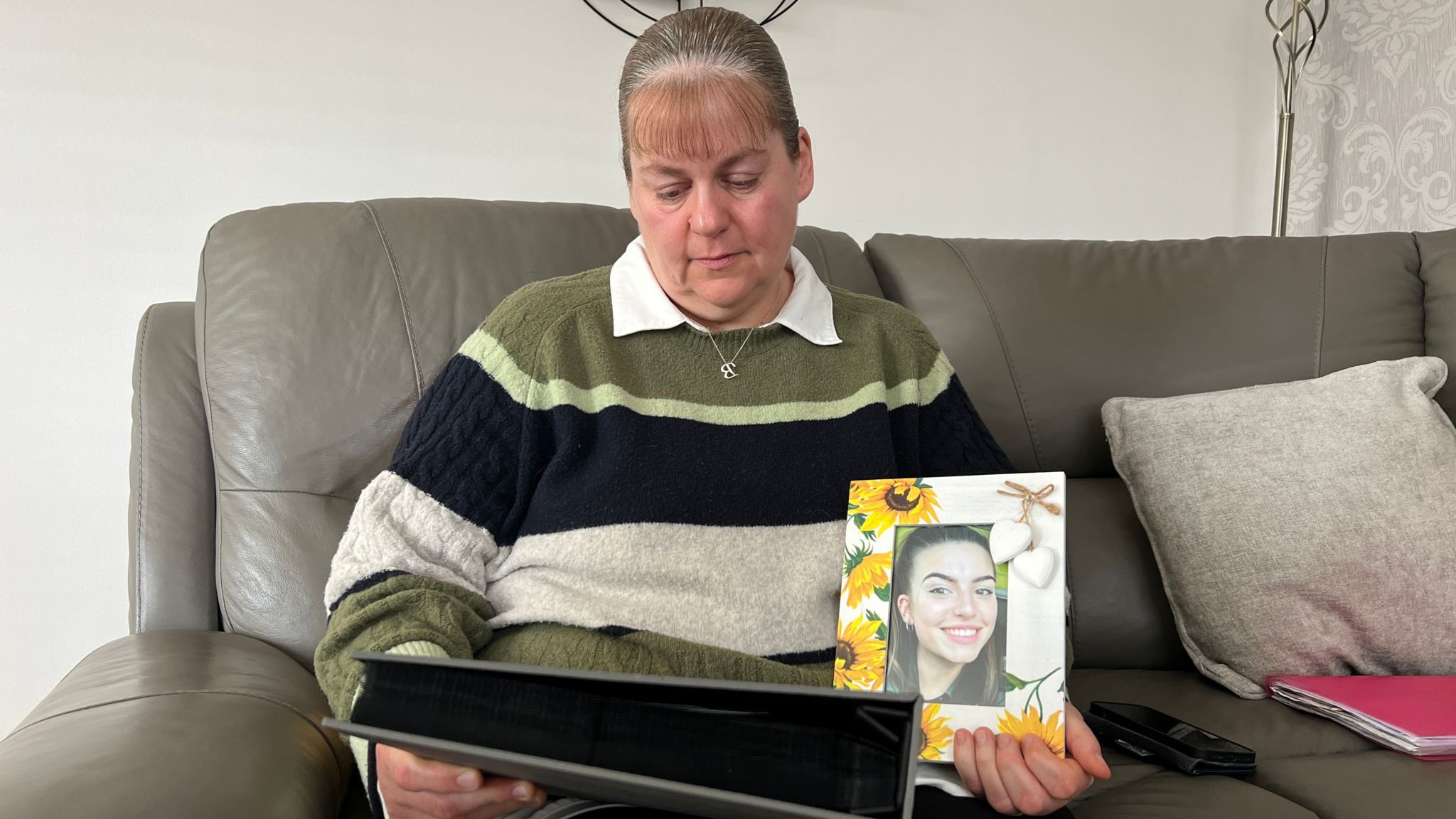 A woman looking at a photo album while wearing a stripy jumper and holding a photoframe of her daughter