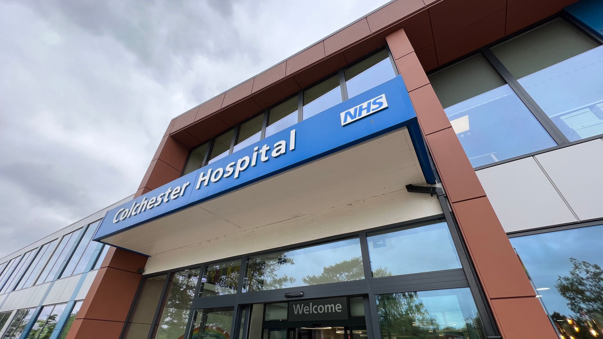 A glass sliding door at the entrance to Colchester Hospital with the word "welcome" above it