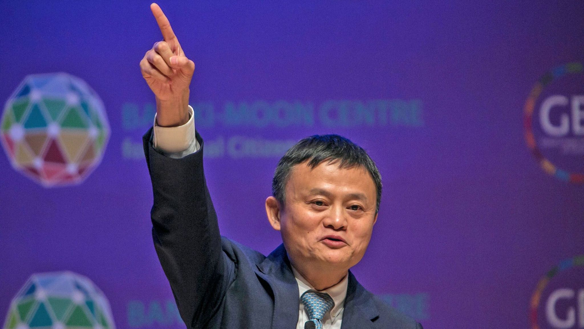 A suited Jack Ma points in the air in a triumphant gesture 