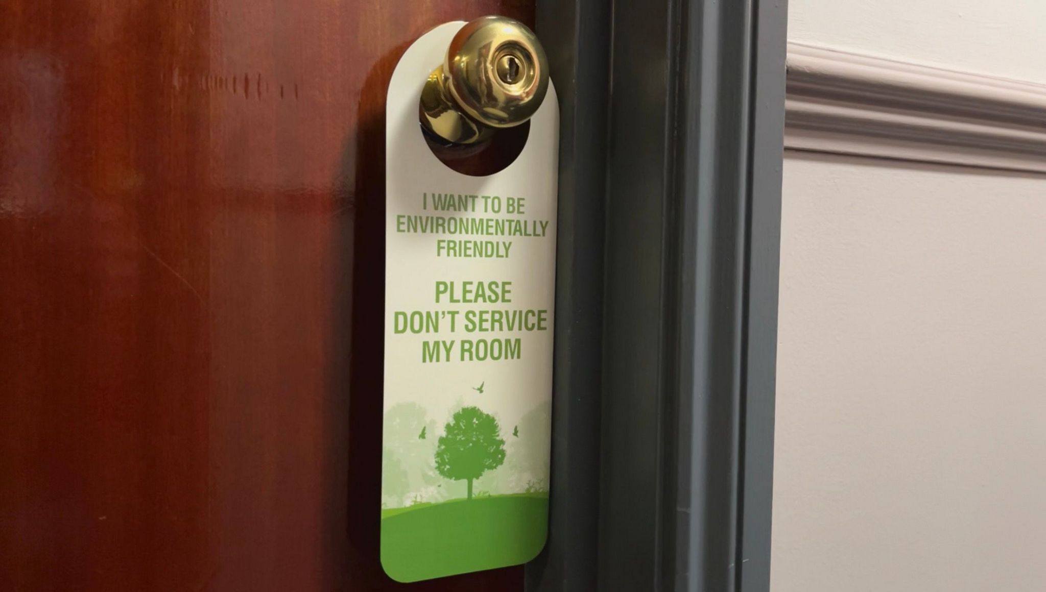A door handle sign that says 'I want to be environmentally friendly. Please don't service my room' hanging on a door