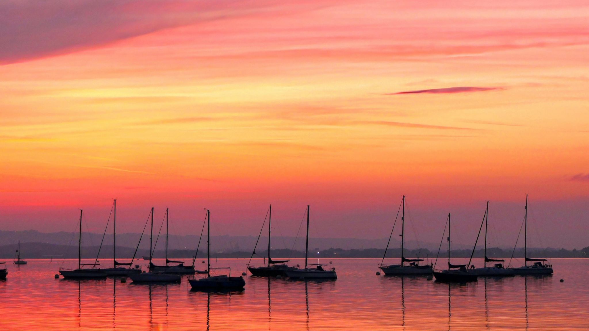 A view looking out to the sea from Gosport with eight boats silhouetted by a bright orange sunset 