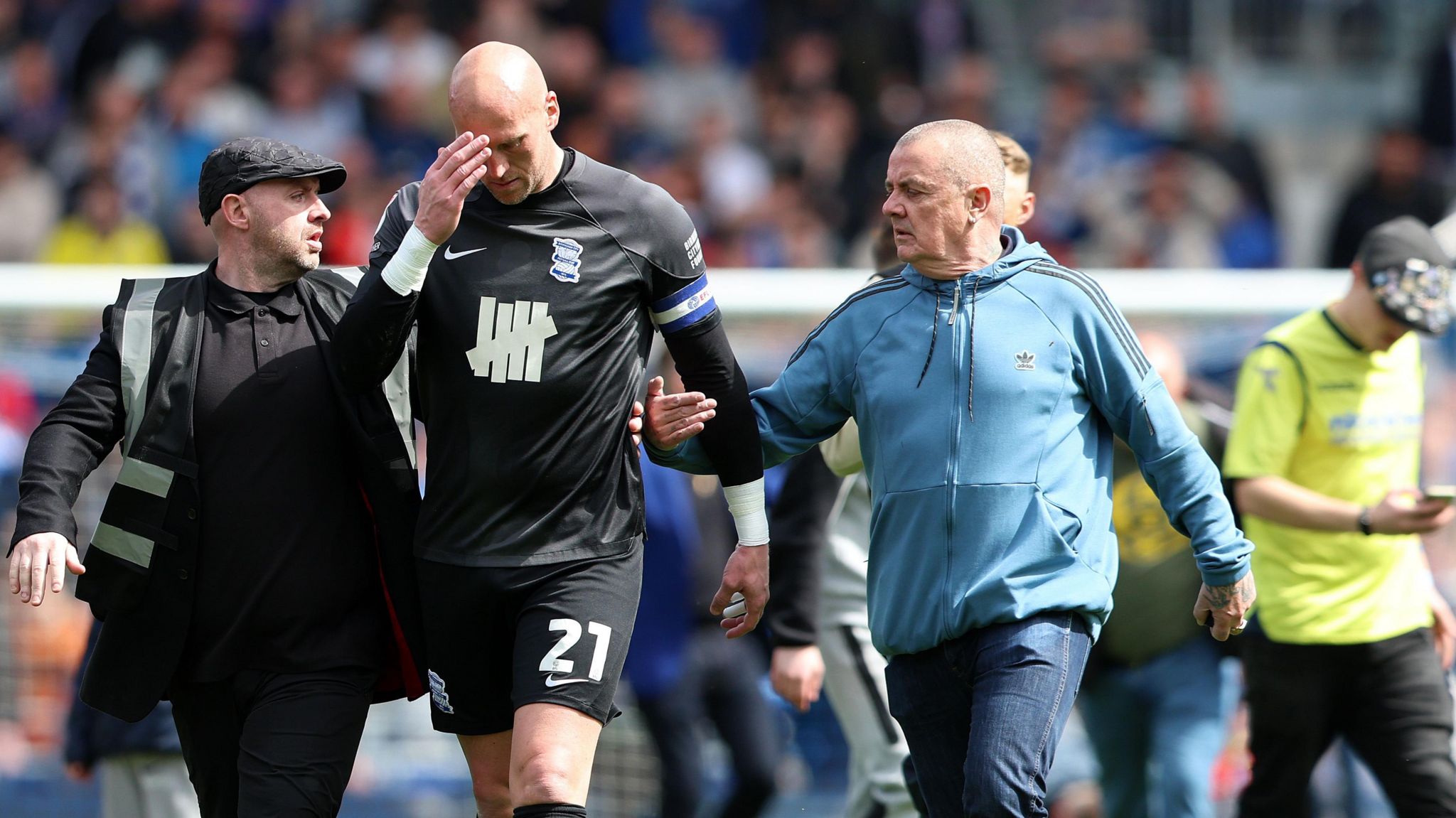 Goalkeeper John Ruddy puts his hand to his head while he is confronted by a fan on his left with a security guard to his right.