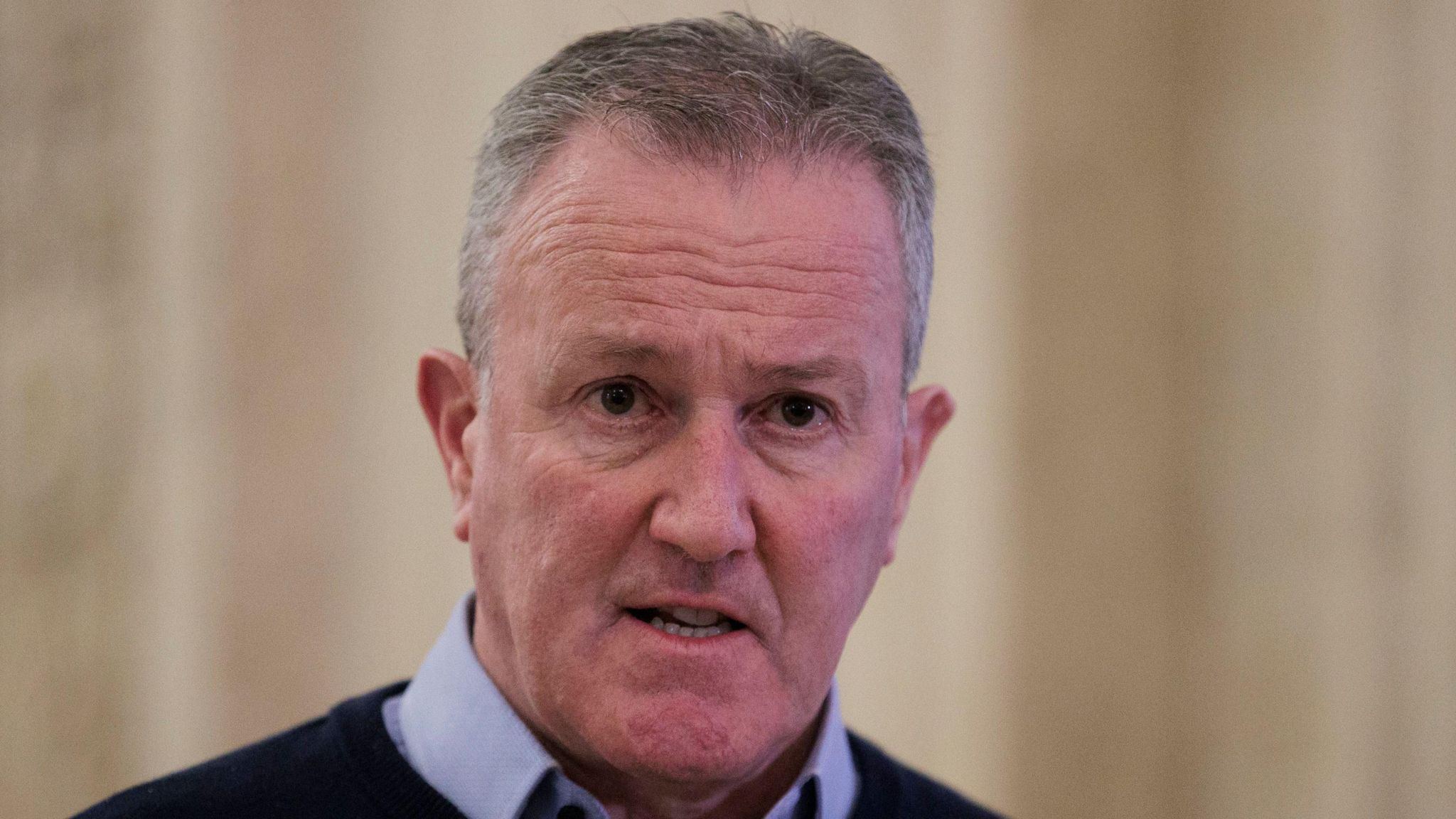 Conor murphy is wearing a shirt under a navy jumper. He's standing in the hall at Stormont.