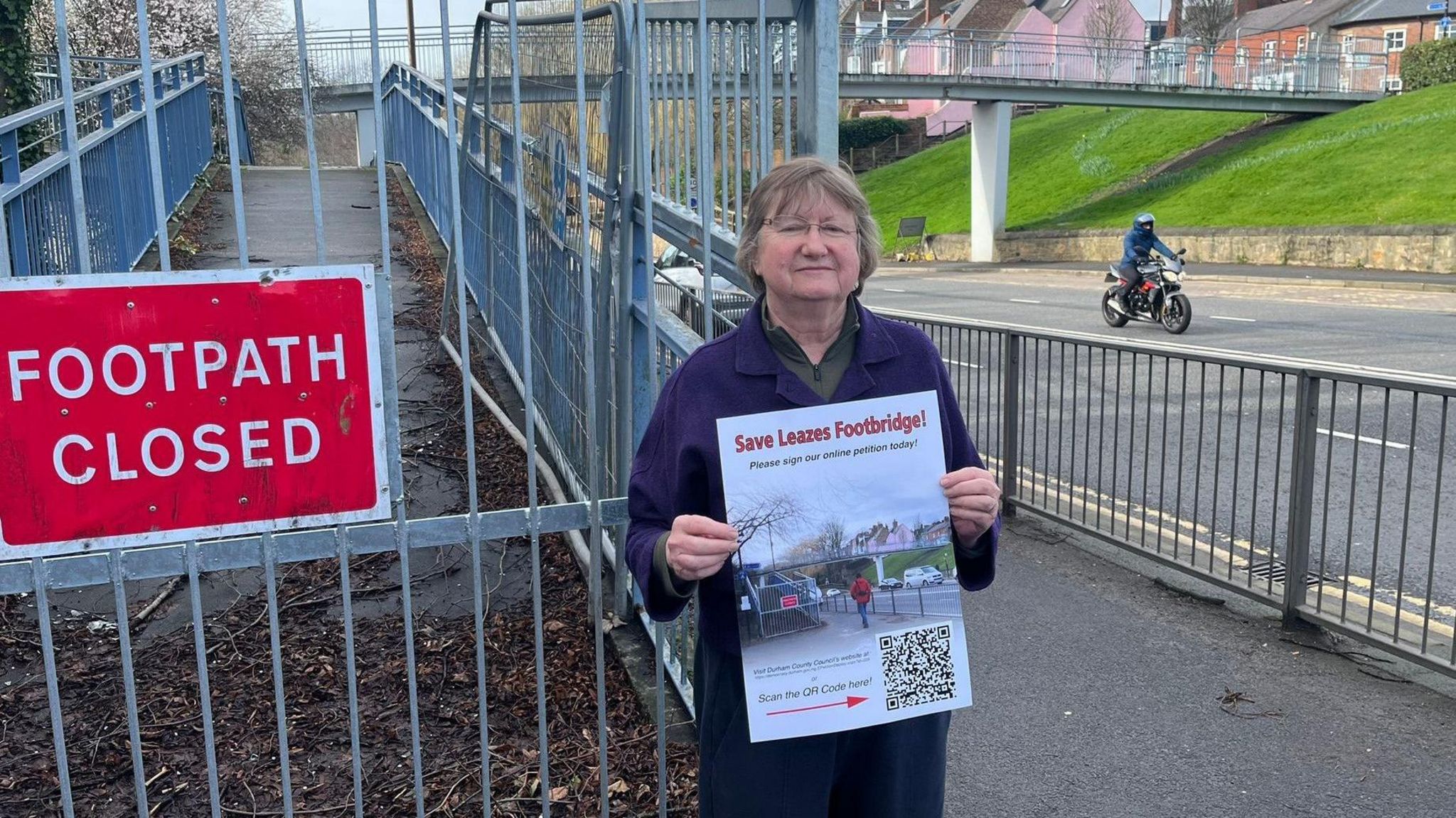 A picture of a woman standing in front of a footpath holding a poster saying Save Leazes footbridge
