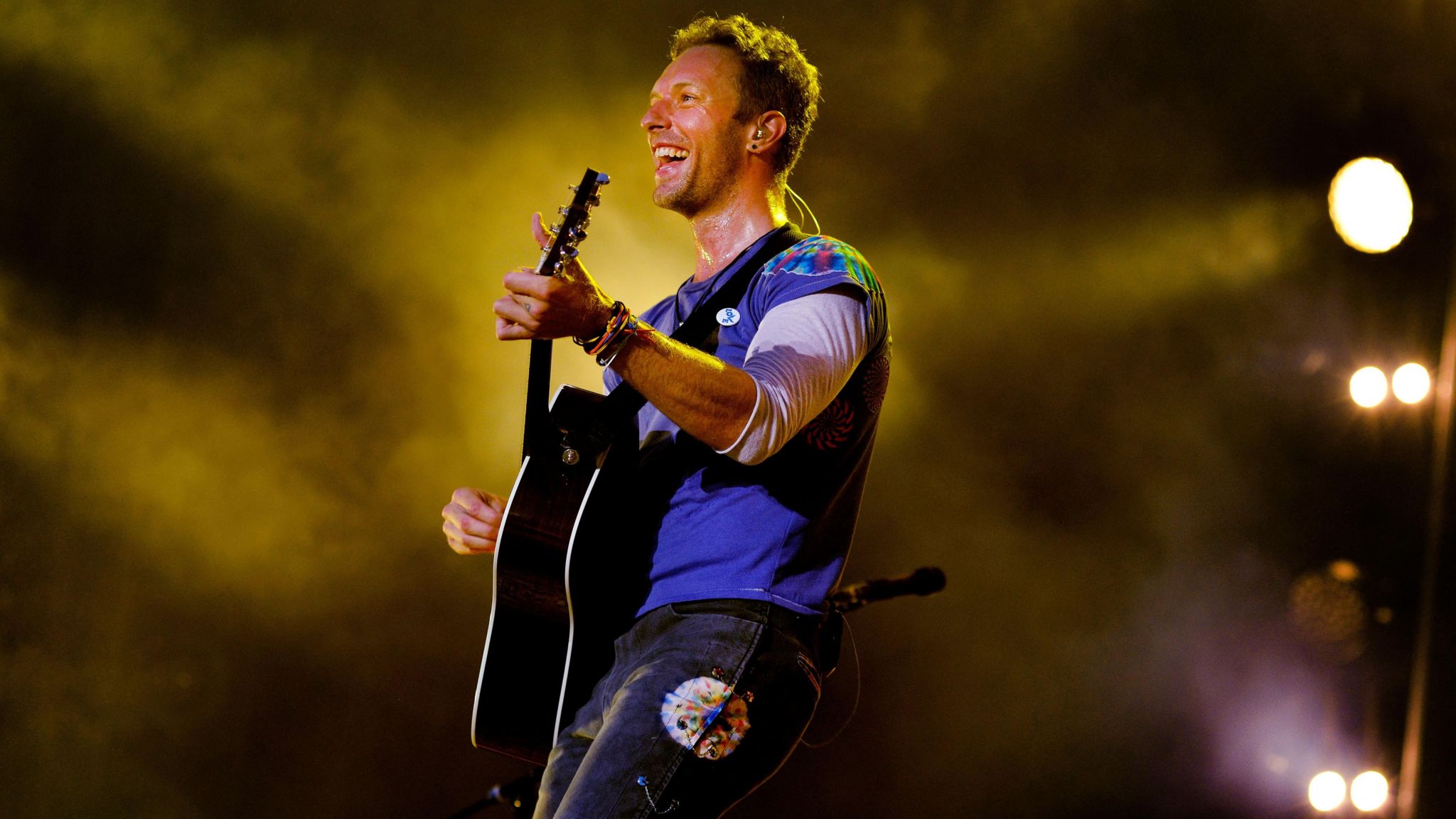 Chris Martin performing with a guitar and surrounded by yellow light