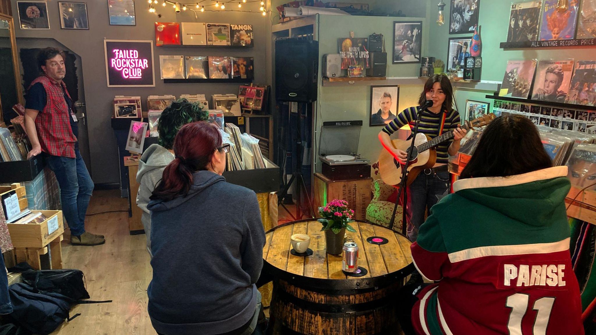 A guitarist is sitting on a stool singing to coffee shop customers