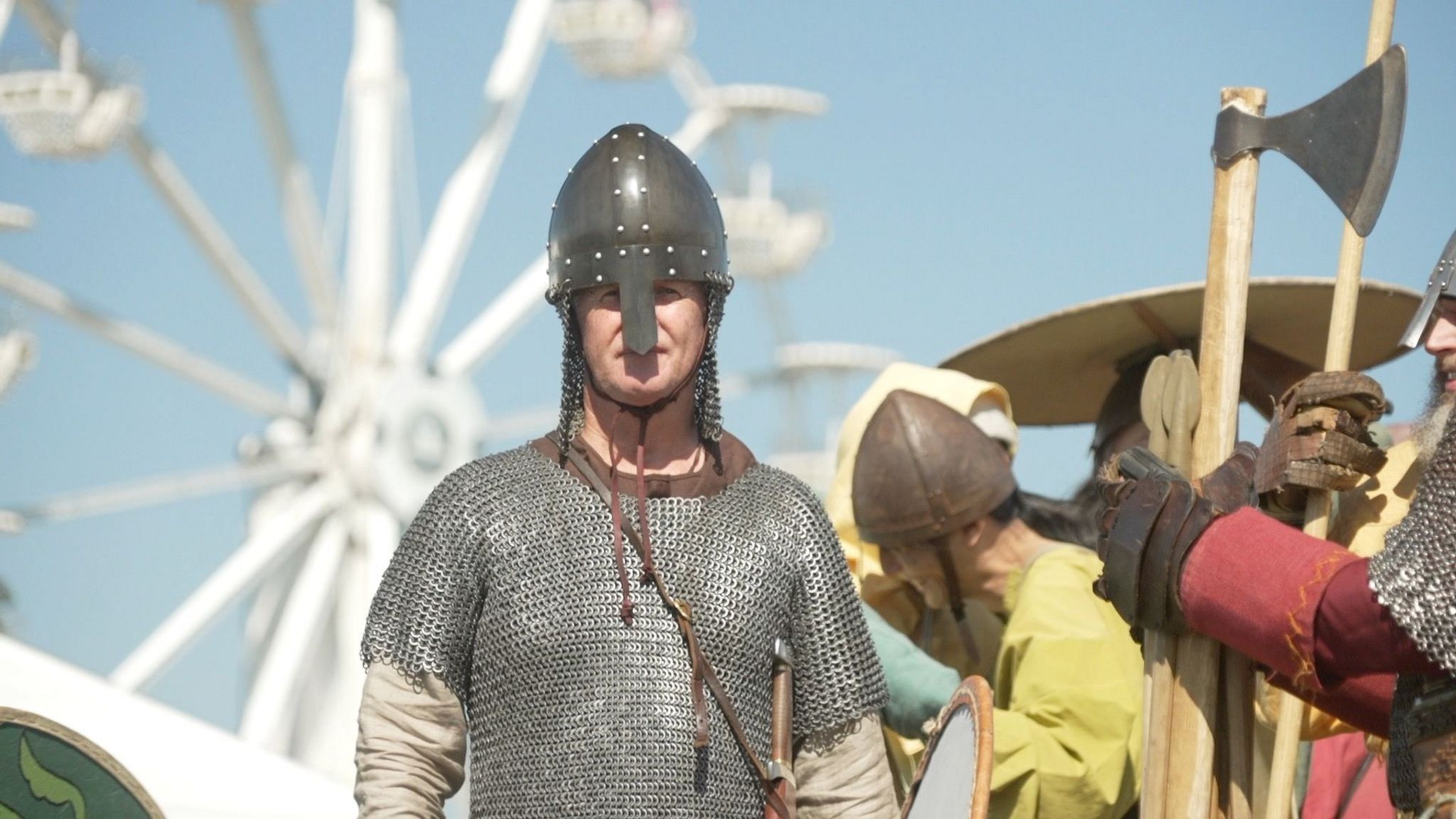 Man dressed as a viking soldier in silver armour and helmet, with a sword hung across him. 