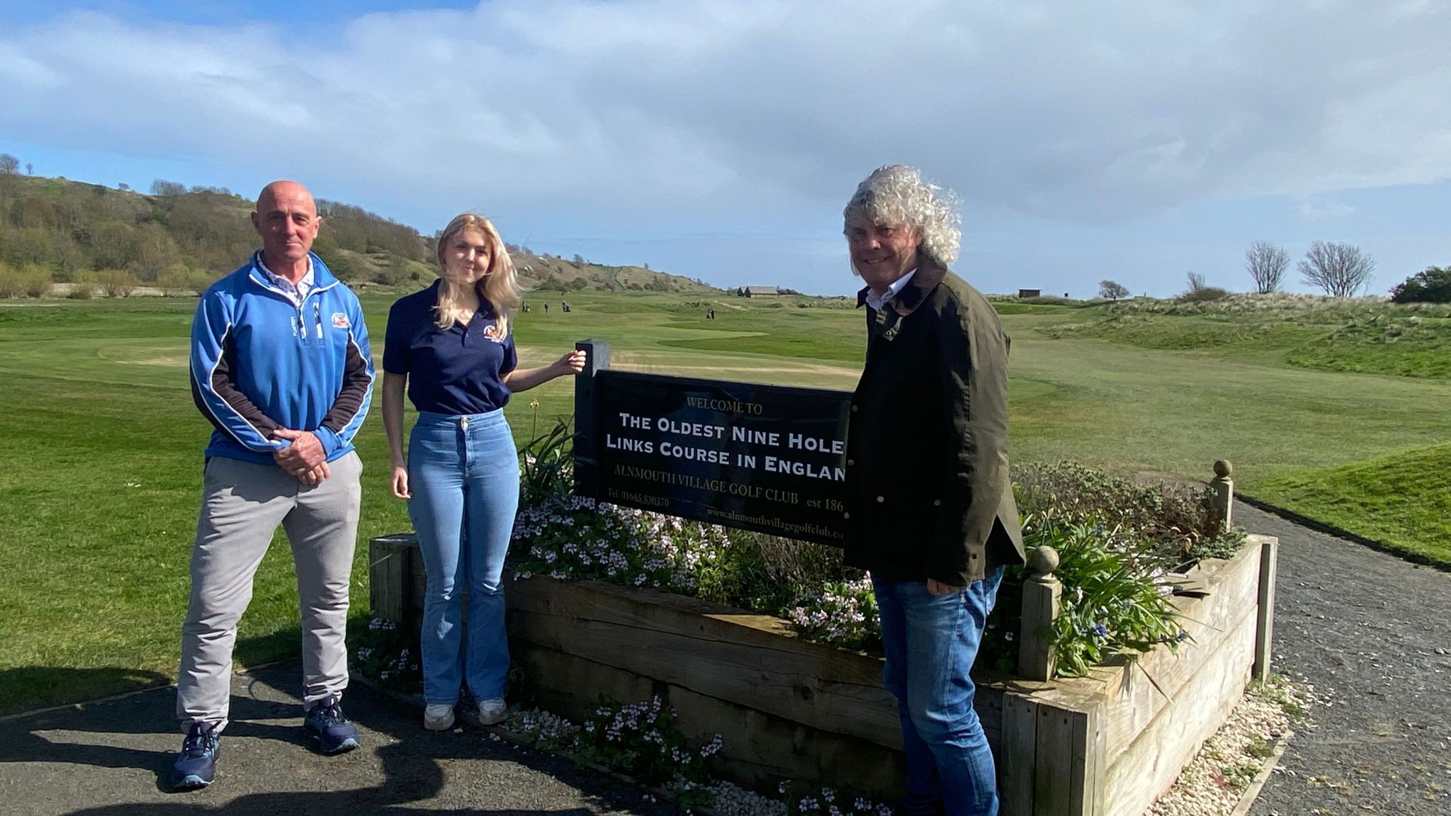 Three people gathered around a sign which says The Oldest Nine Hole LinksCourse in England