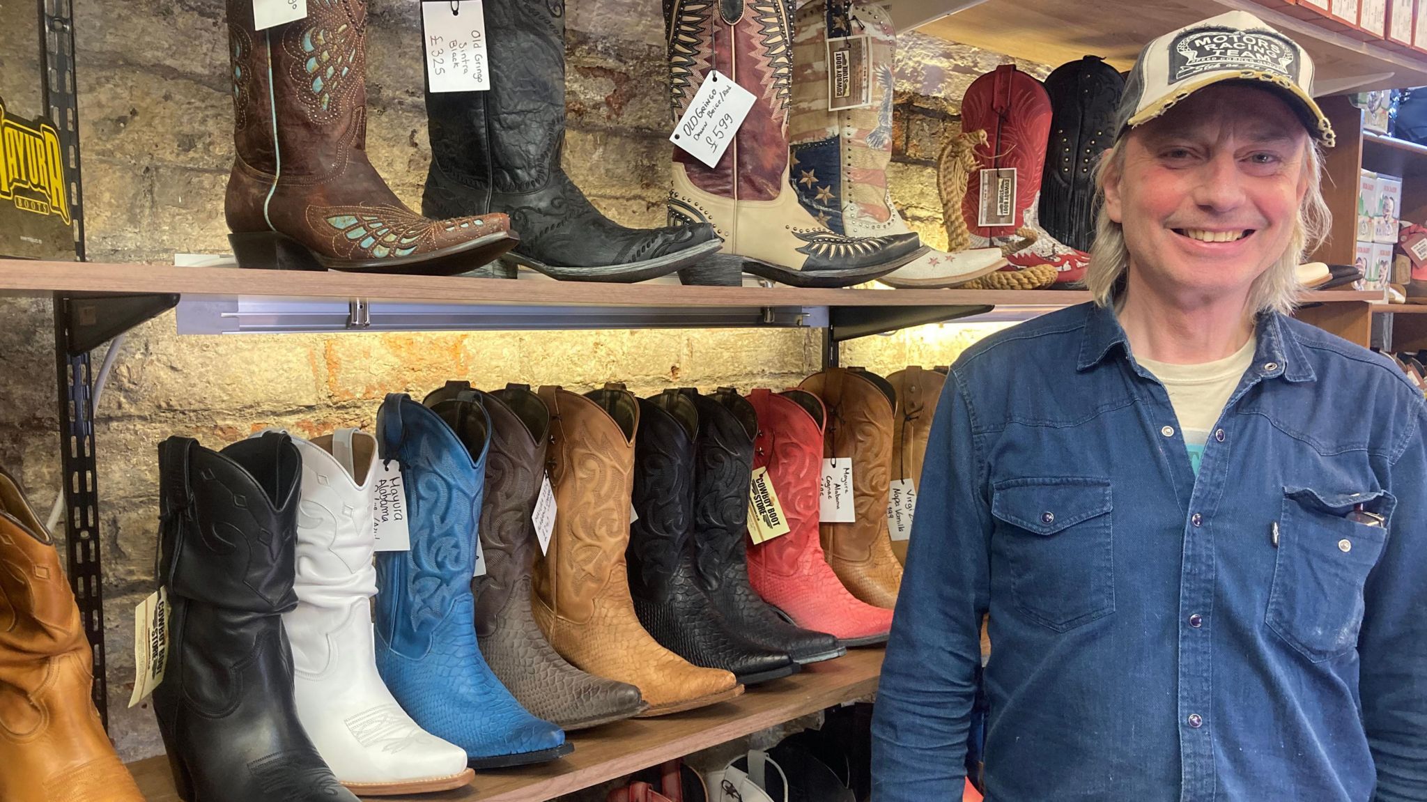 Pete Tooley in a blue denim shirt and baseball cap next to shelves of boots