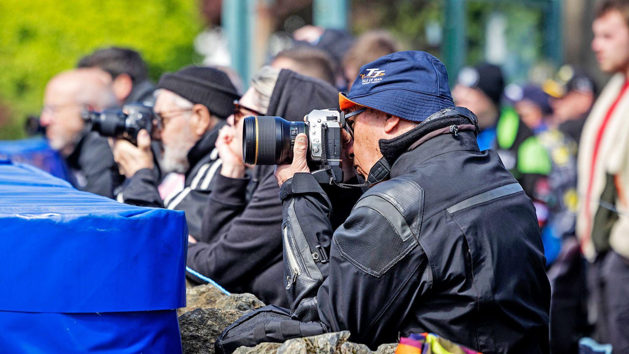 People with cameras pointed ahead sitting behind a barrier
