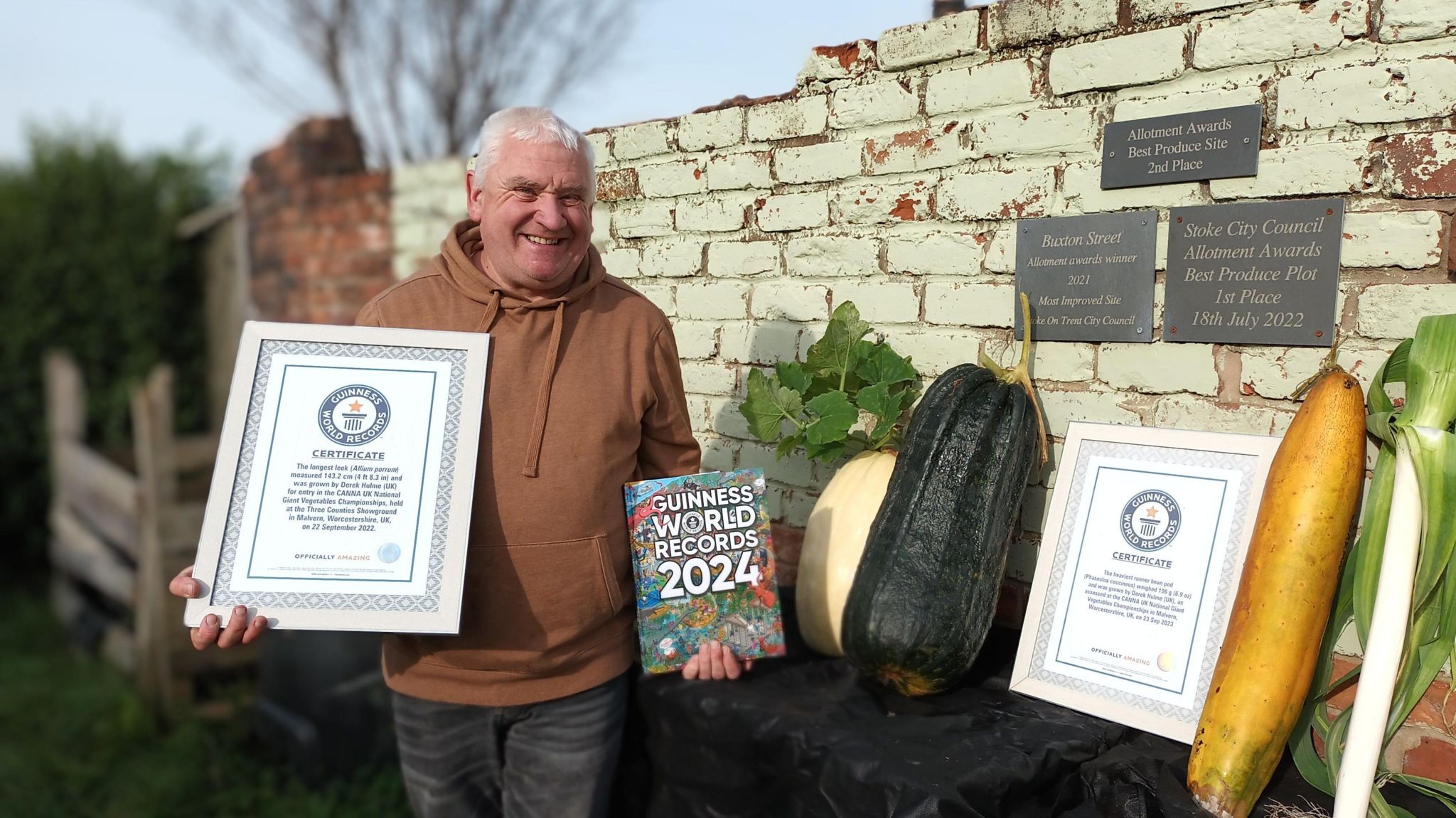 Derek Holme is surrounded by large vegtables and two Guinness world record certificates He is also holding the Guinness Book World Records 2024.