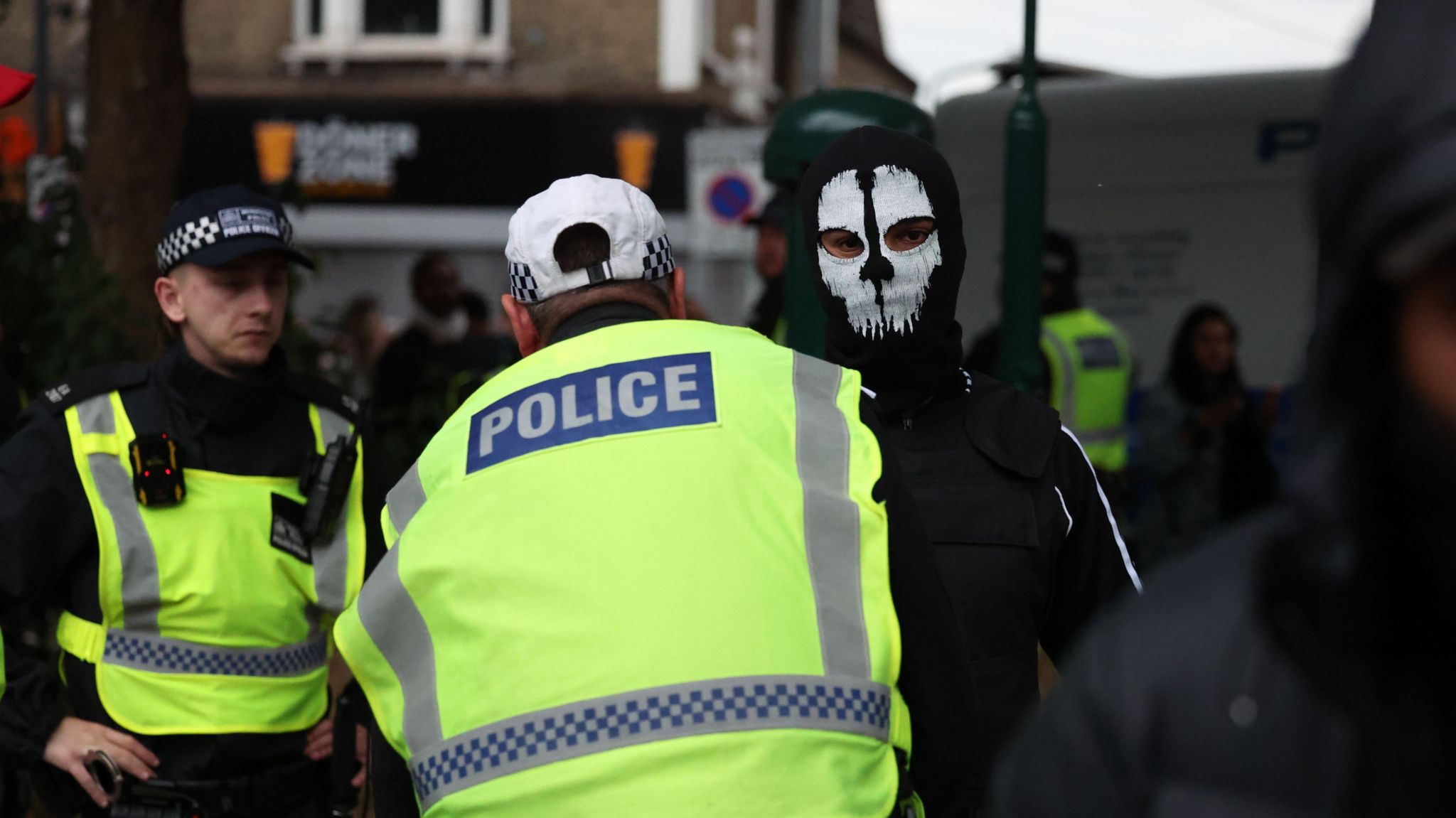 A police officer searches a masked person in Walthamstow on 7 August