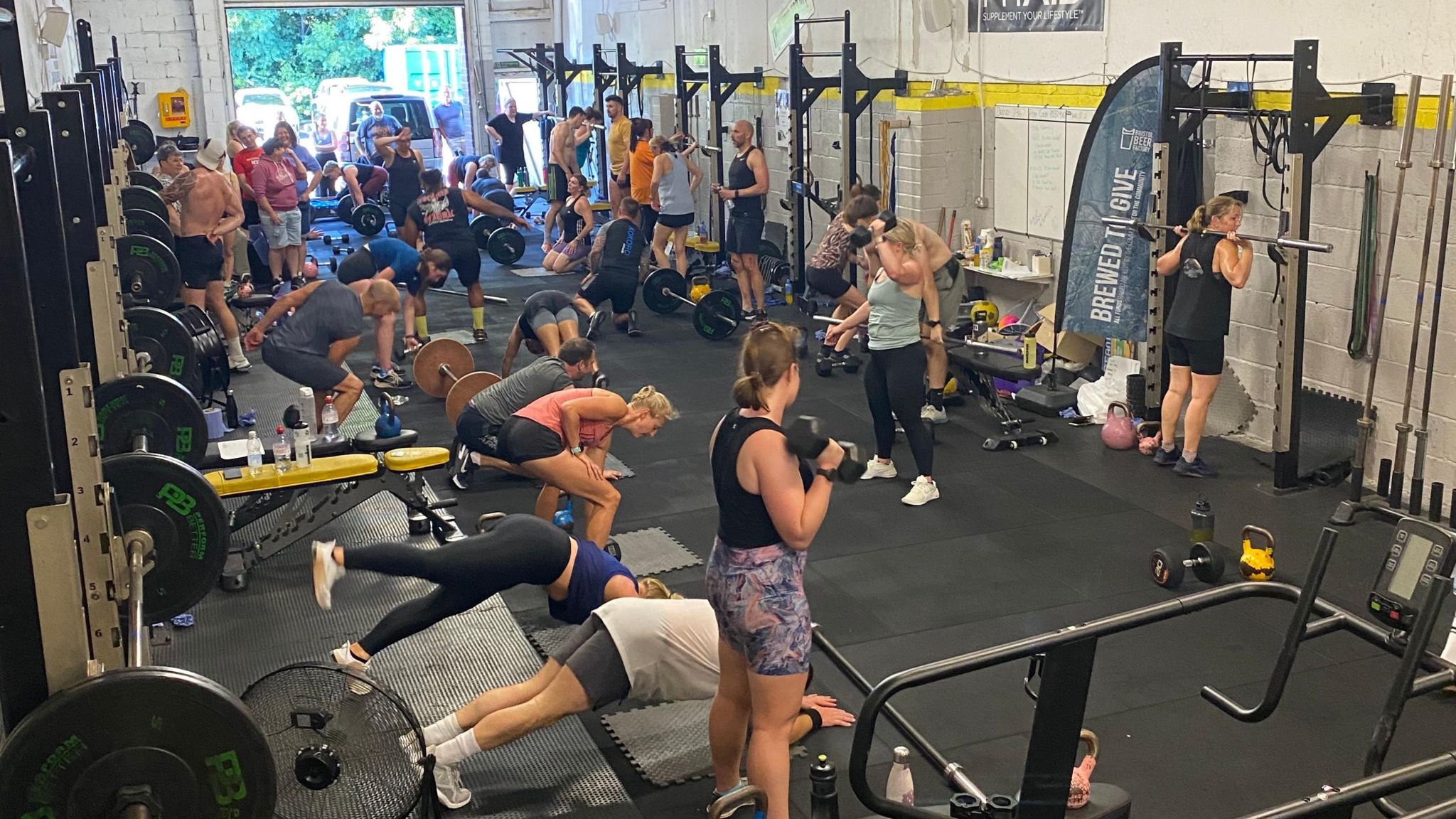 Image of lots of people working out at a gym. Some are lifting weights, some at doing stretches on the floor. 