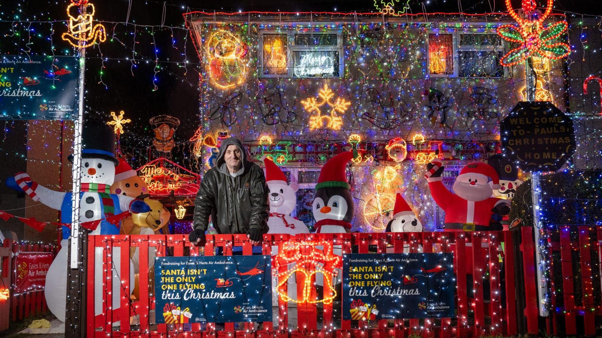 Paul Bibby wearing a black raincoat and standing in front of him home which is covered in Christmas lights