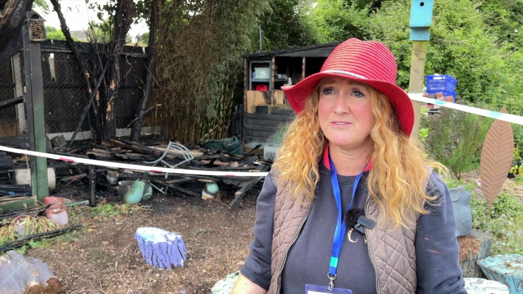 Catherine Waters-Clark wearing a red had stood in front of the burnt remains of some garden furniture.