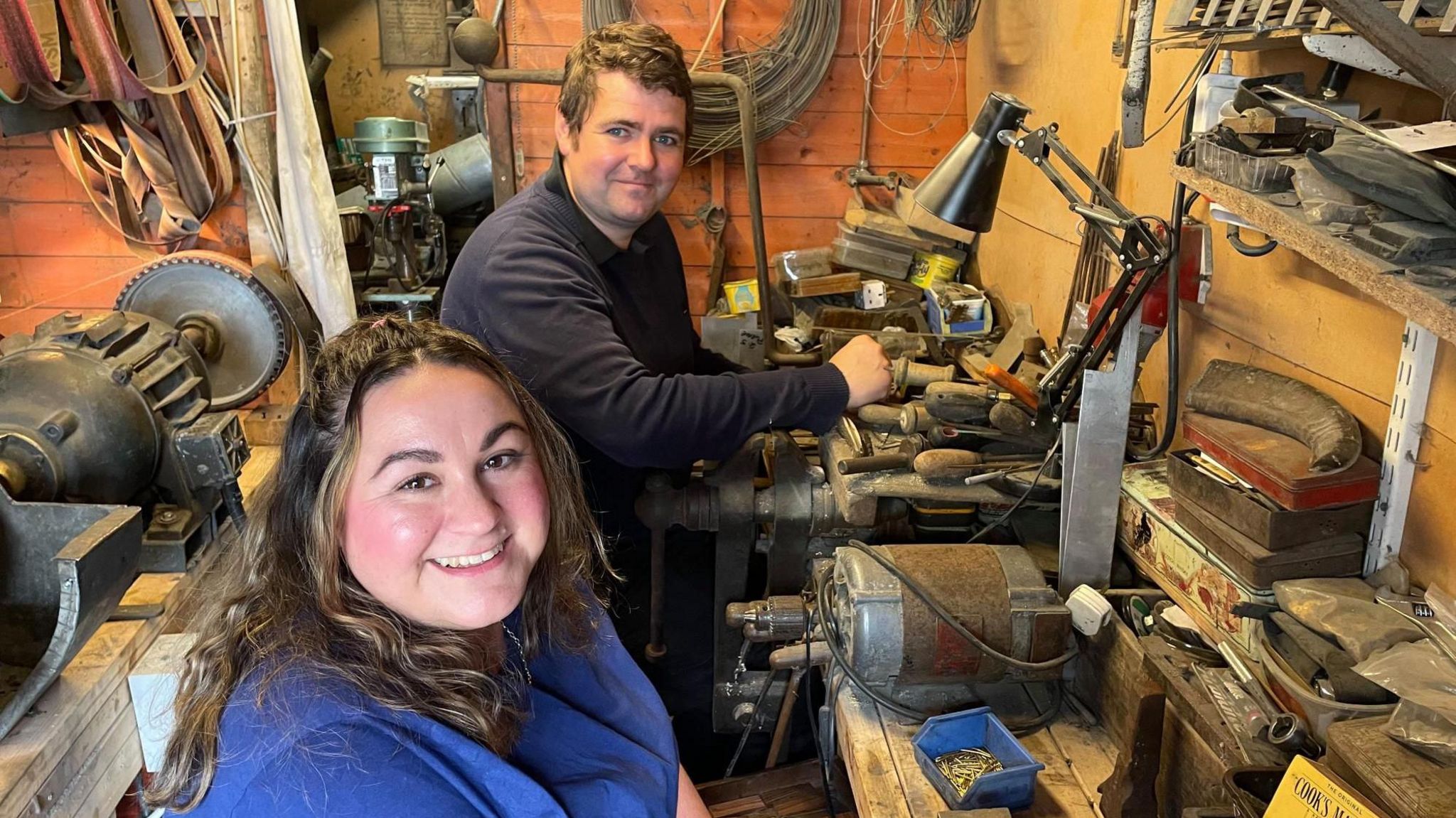 A man and woman sit next to each other in a shed surrounded by old machinery