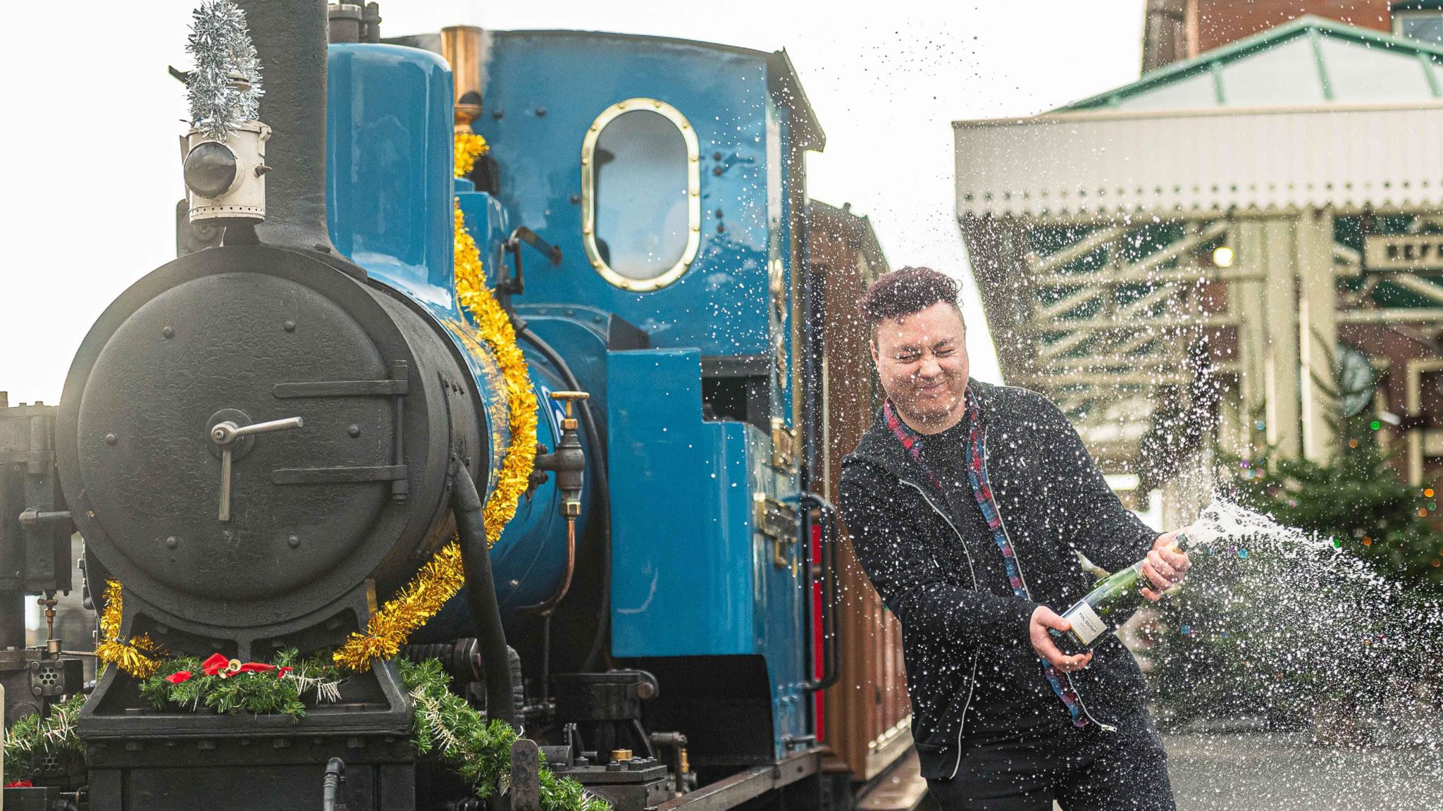 Lottery winner Neil Leighton with a bottle of champagne and a locomotive in the background