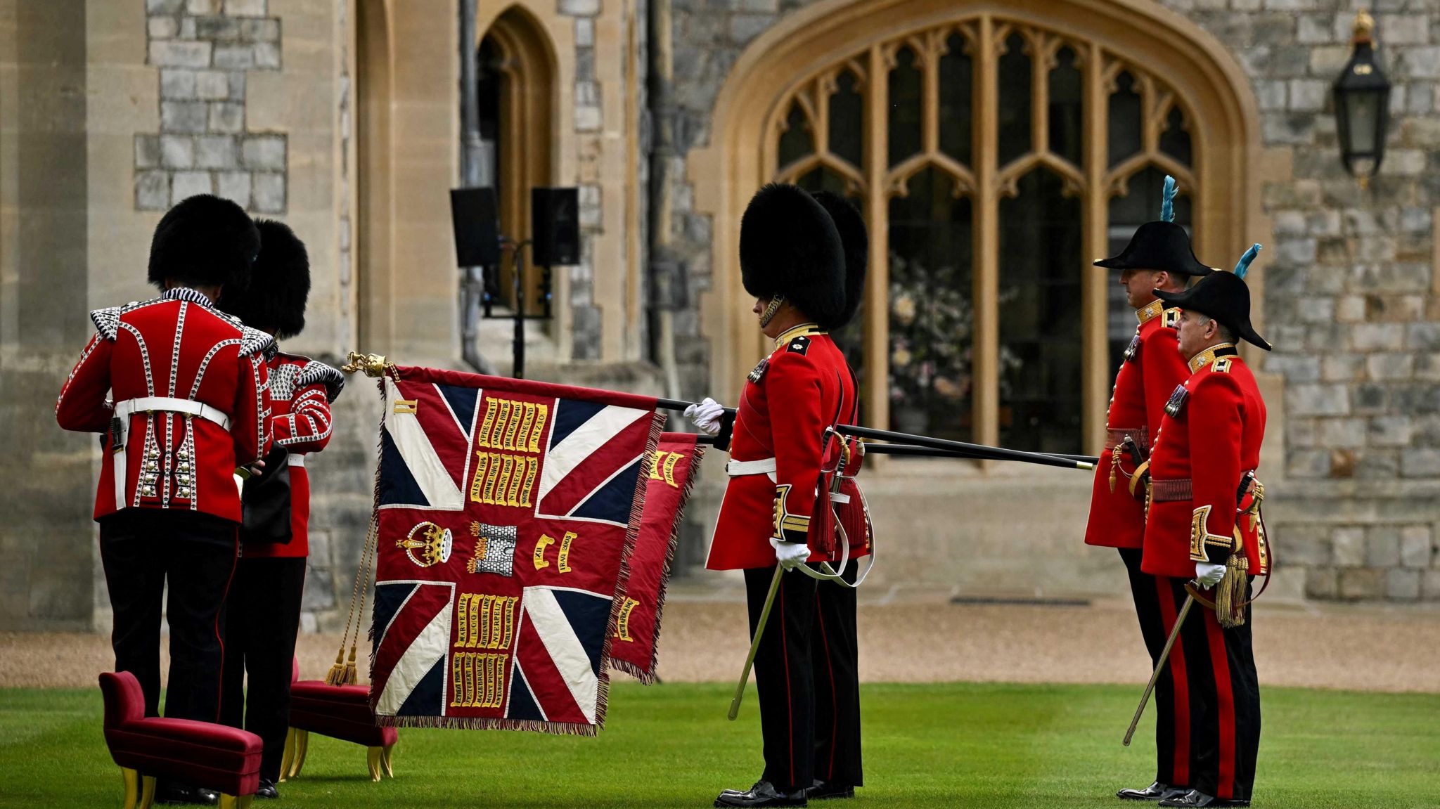 The Irish Guards in full dress - black trousers with a red stripe down each side, a red jacket with military regalia and white belt, plus white gloves and a busby hat. Some car decorative swords and the new flags. Photo taken outside Windsor Castle