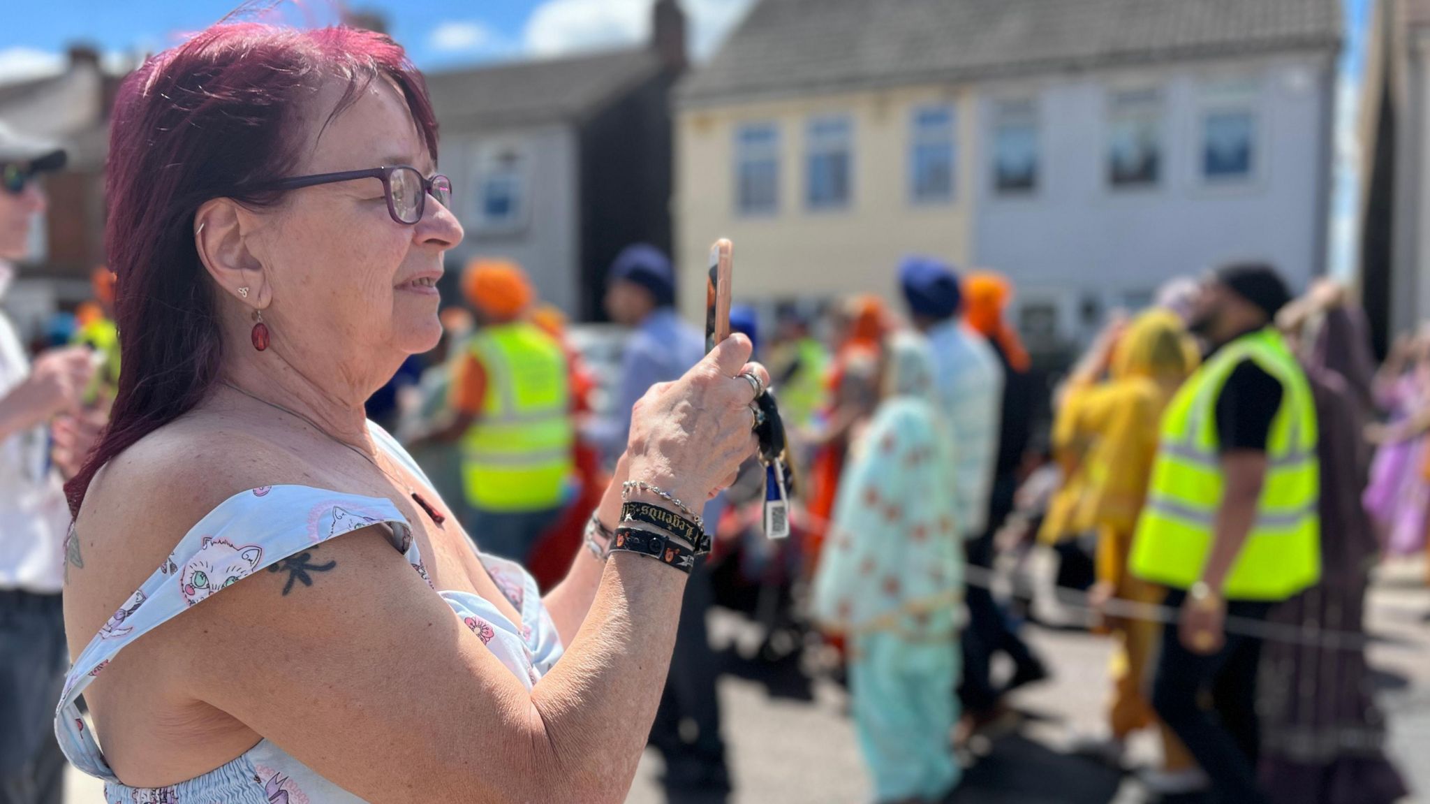 A woman holds up a phone to record a colourful Sikh procession going passed