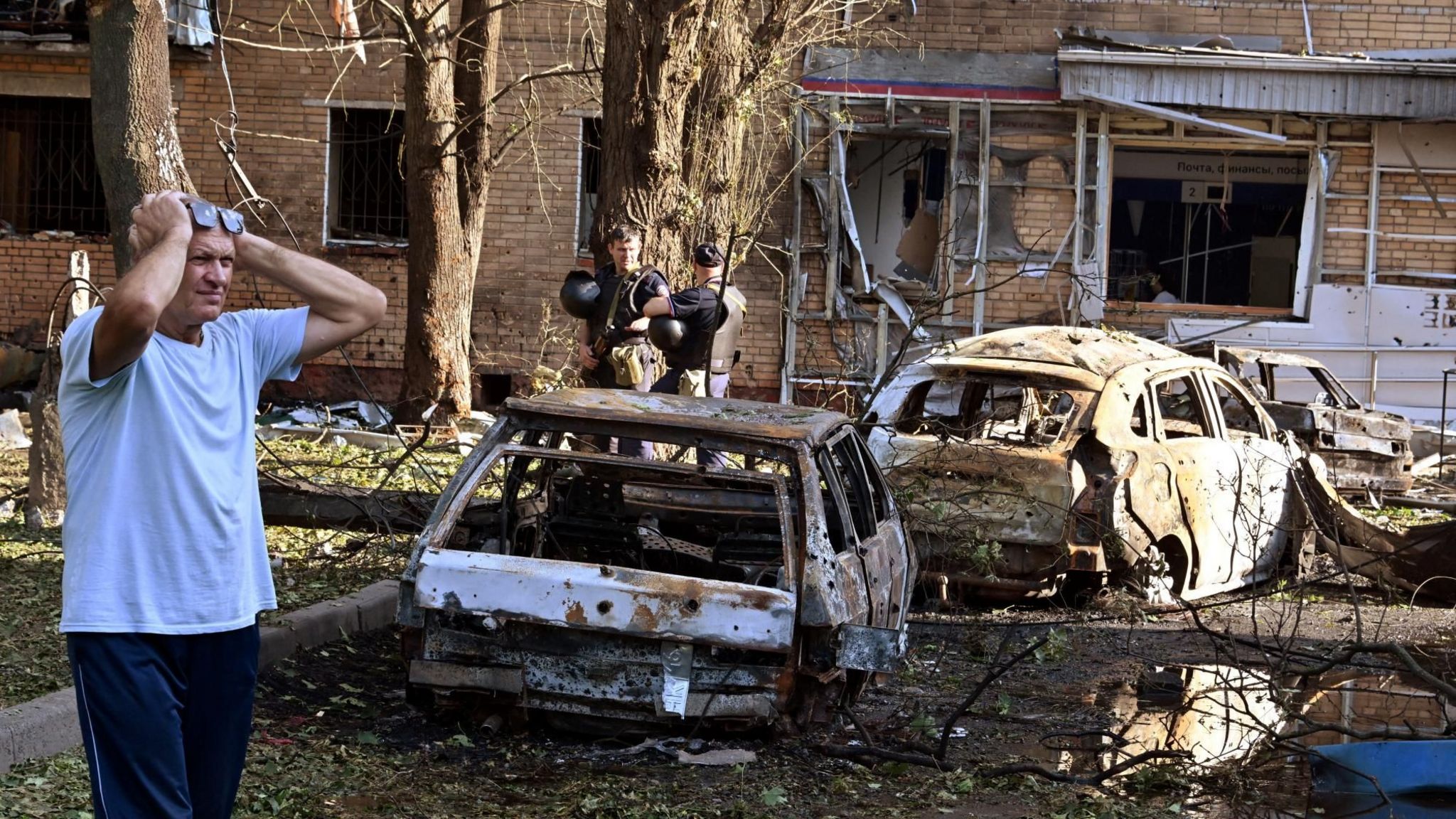 A man reacts while standing next to burnt-out remains of cars