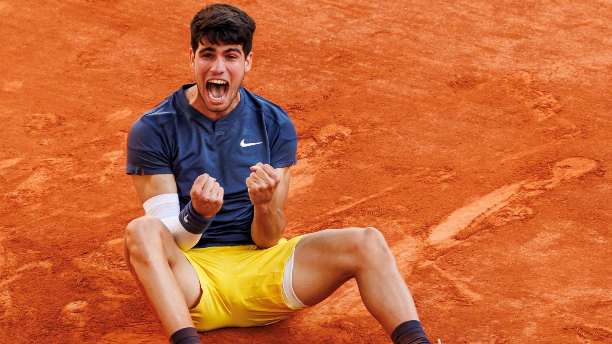 Carlos Alcaraz sits on the Roland Garros clay in celebration