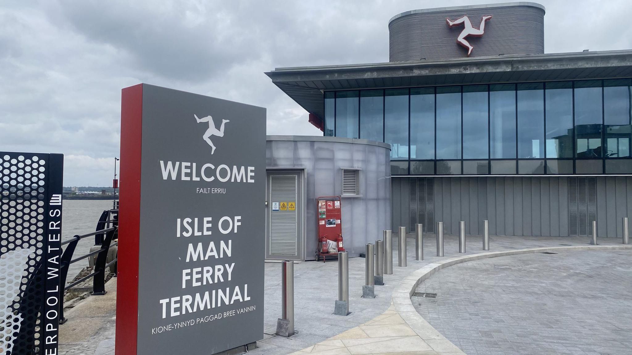 The new Liverpool ferry terminal, a grey building with bollards in front and a sign welcoming passengers to the left of the image 