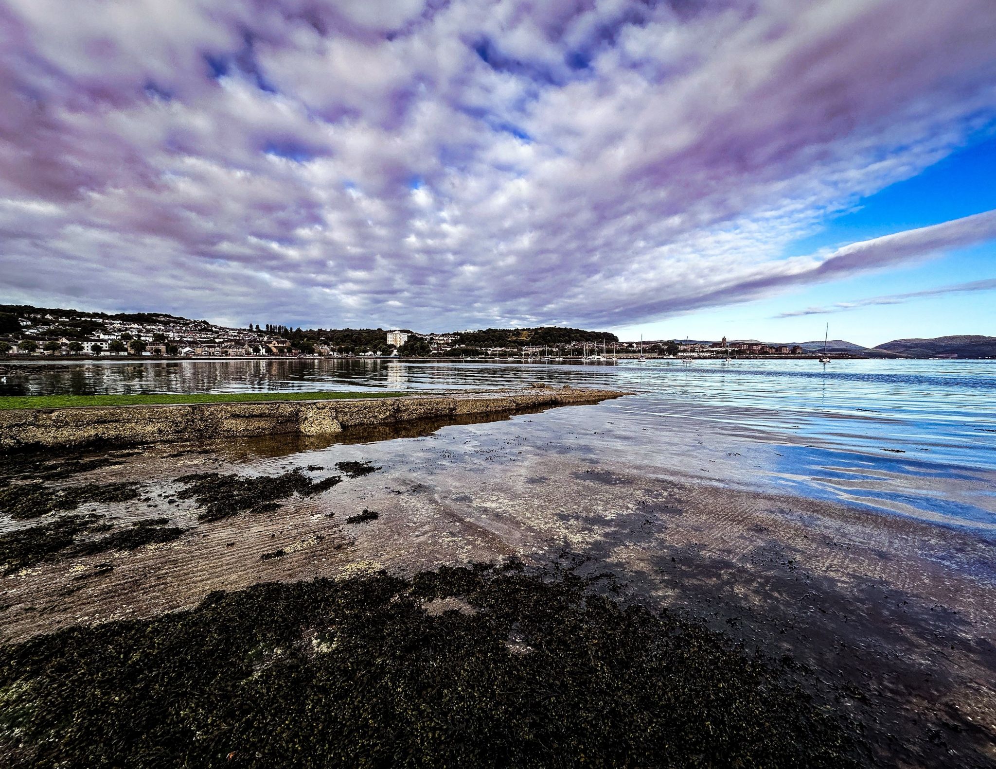 Panoramic image of white clouds over a bay, reflected in the water with houses in the far distance