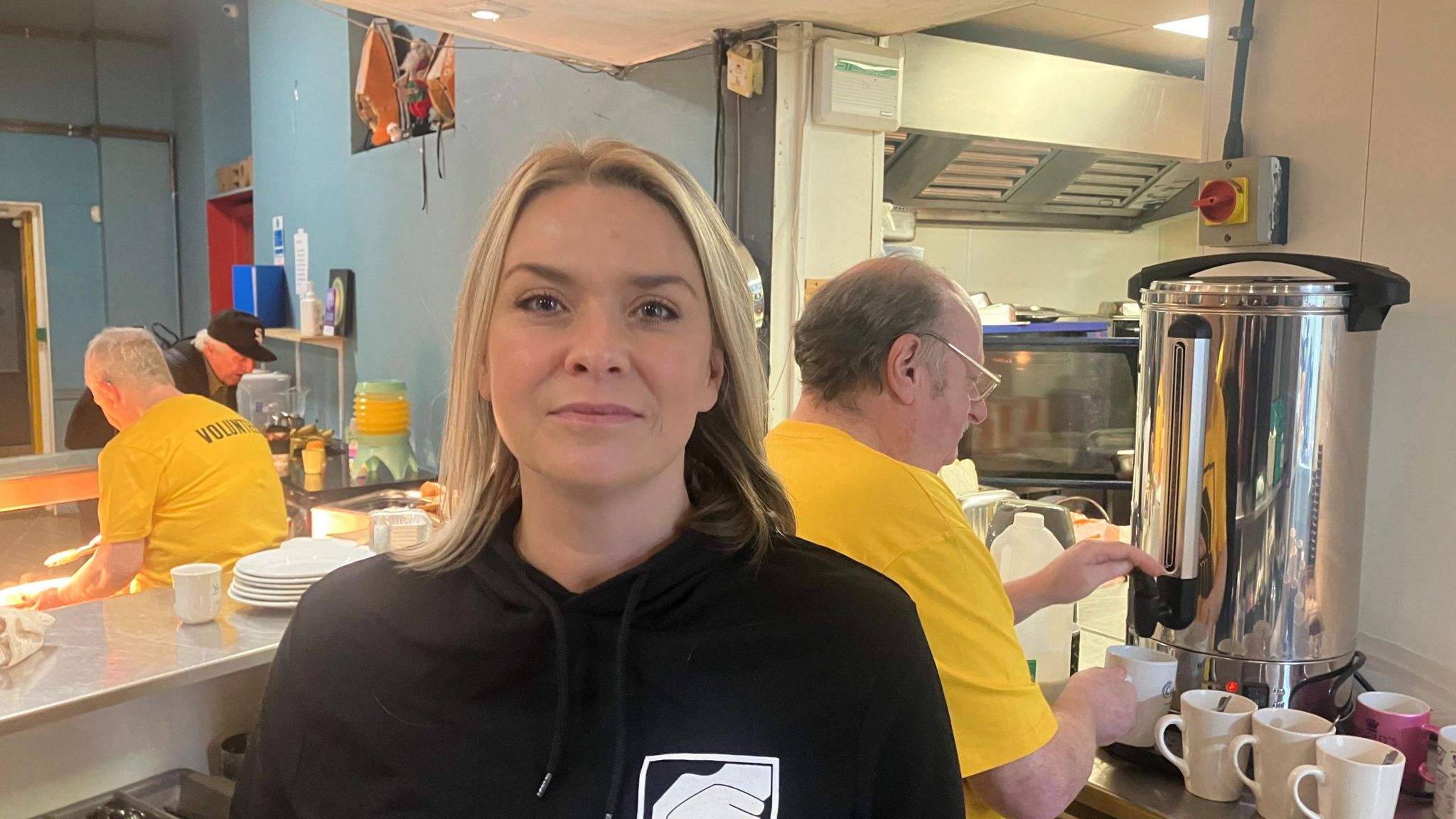 Jane Carroll, Lifeshare trustee, stands in front of a counter where a volunteer is serving hot drinks