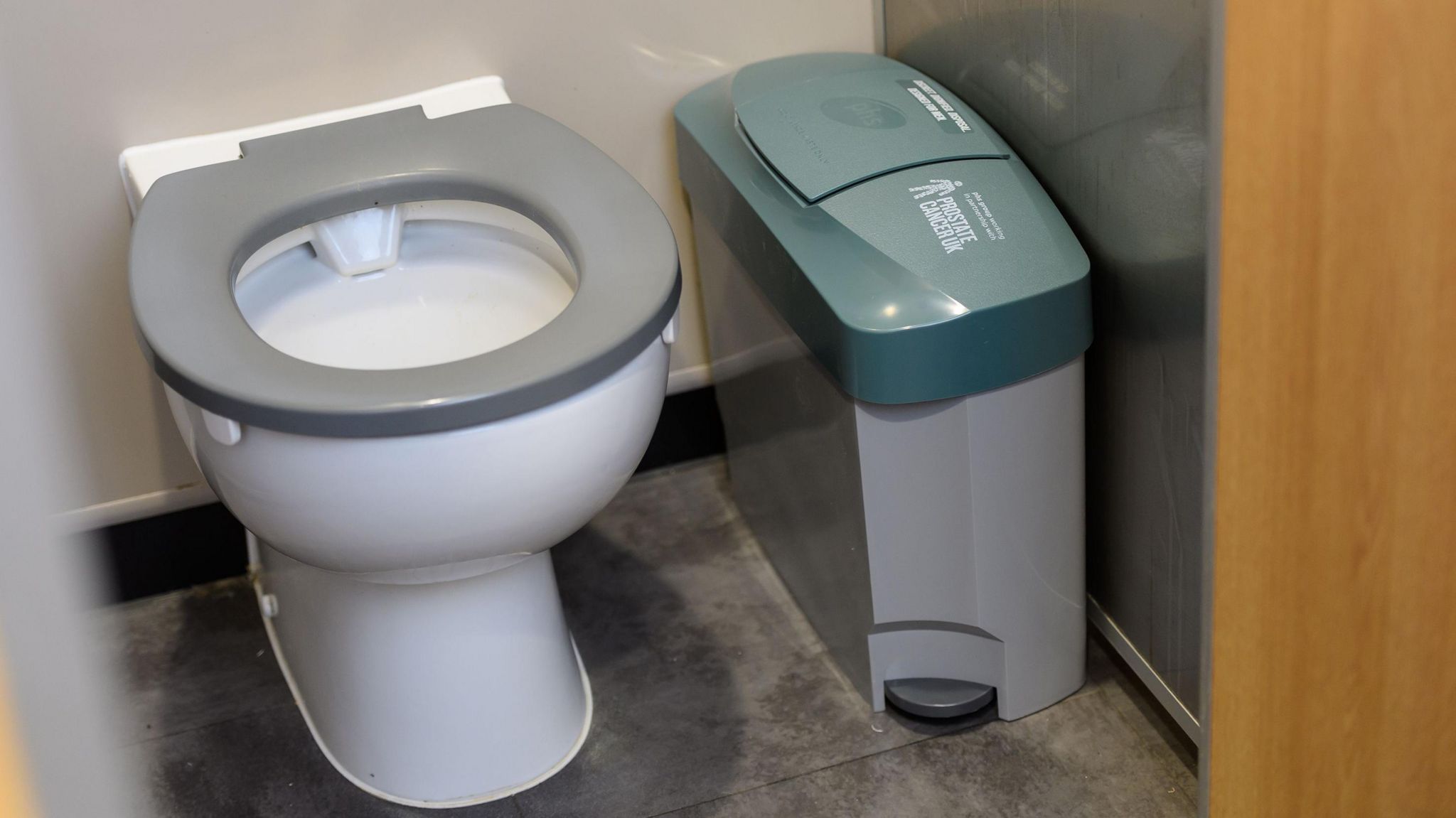 A white toilet next to a grey bin with a green lid