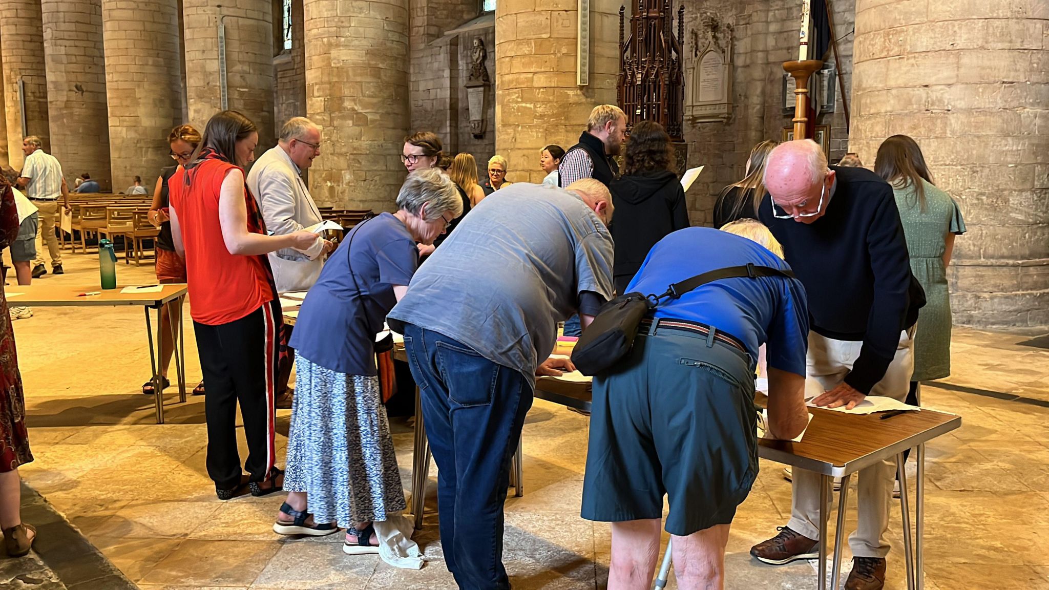 People stood around a table inside Tewkesbury Abbey writing their questions on pieces of paper.