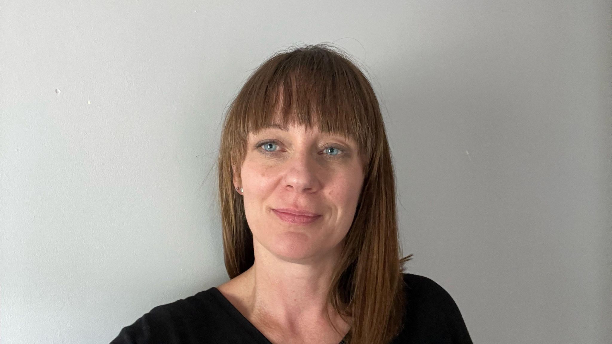 A smiling Kate Haley looks directly at the camera, she has brown hair and is wearing a dark top