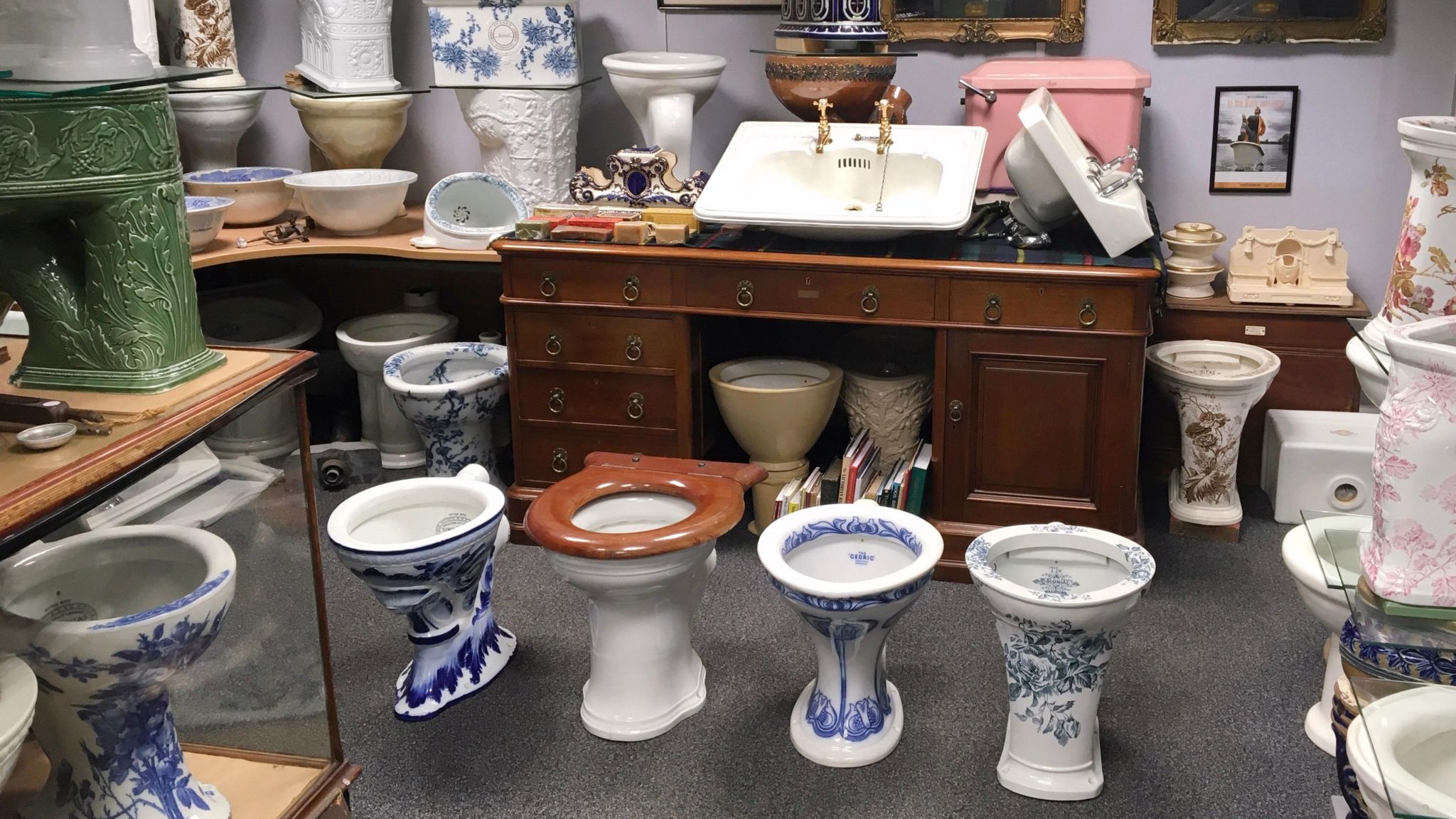 A room full of antique loos, sinks and basins with ornate carvings and floral prints