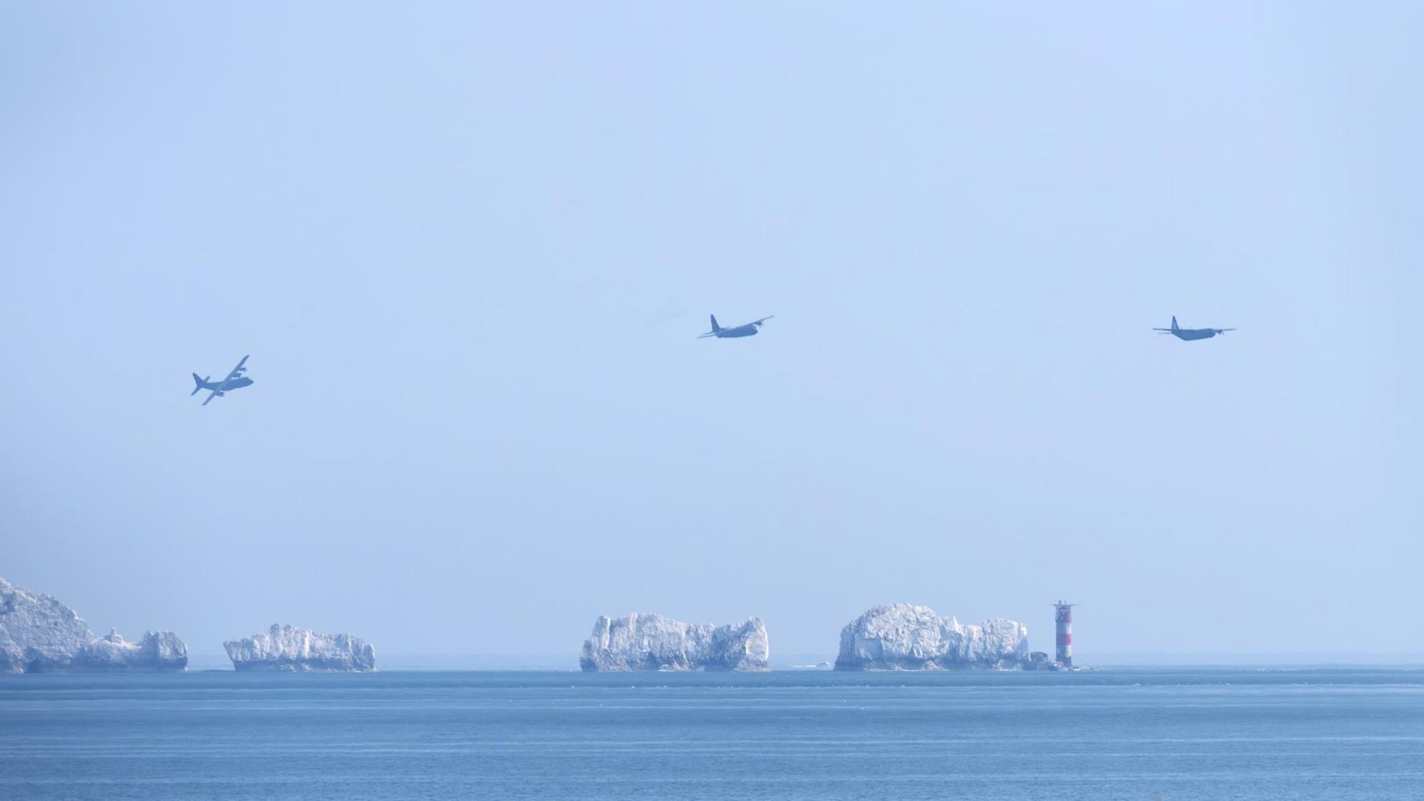 Three Hercules aircraft flying over The Needles lighthouse