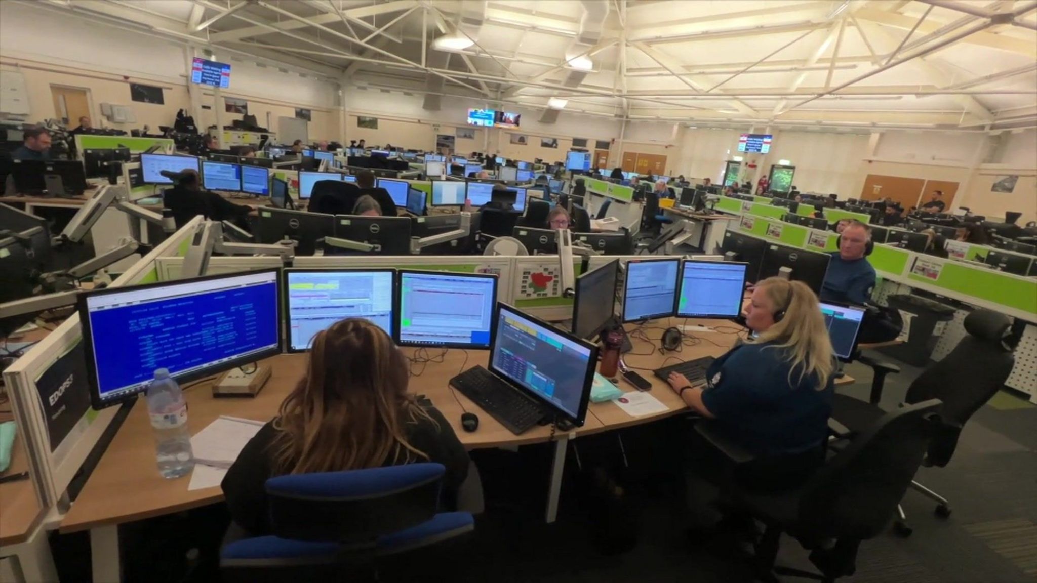 A large room with a number of desks and computers, with people sat at them wearing headsets 