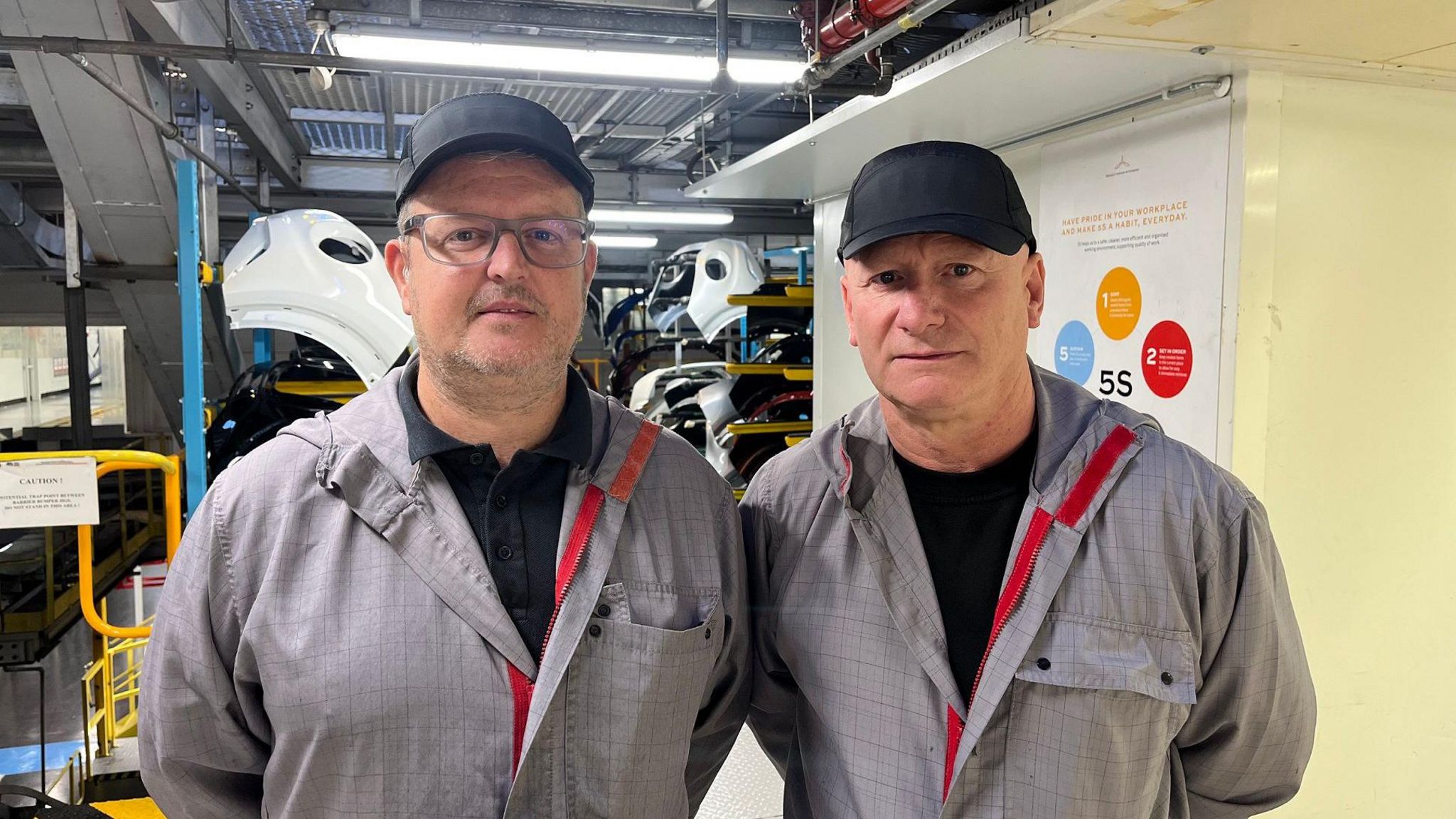 Nissan workers Michael Connolly (left) and Gowan Kirkley. Both men are wearing grey overalls and black caps.