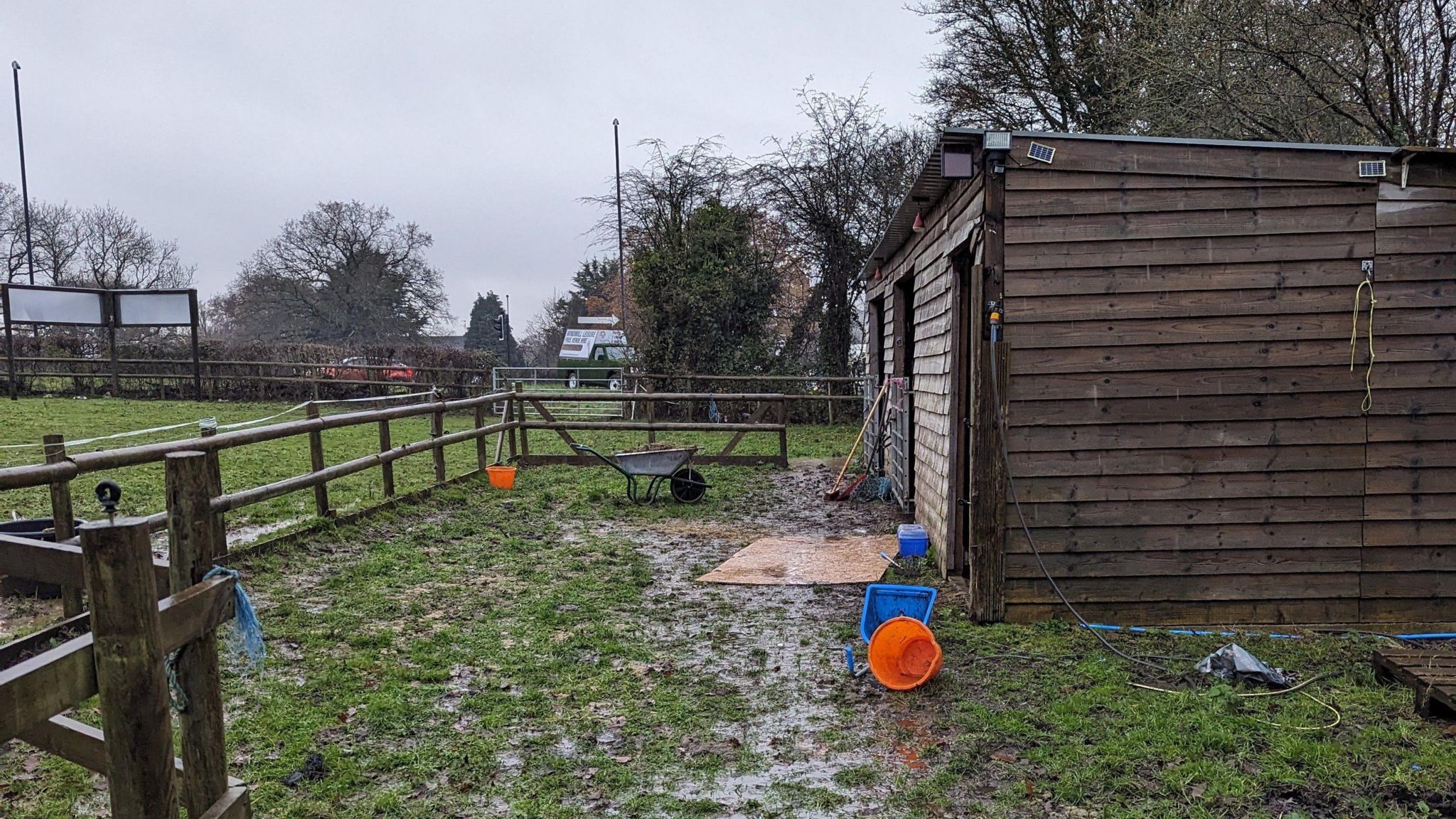 A muddy field in Westerleigh where Shane Paul Sims kept his two horses. A small stable building can be seen, with a wheelbarrow and other supplies nearby. There is a fence around the small area. 