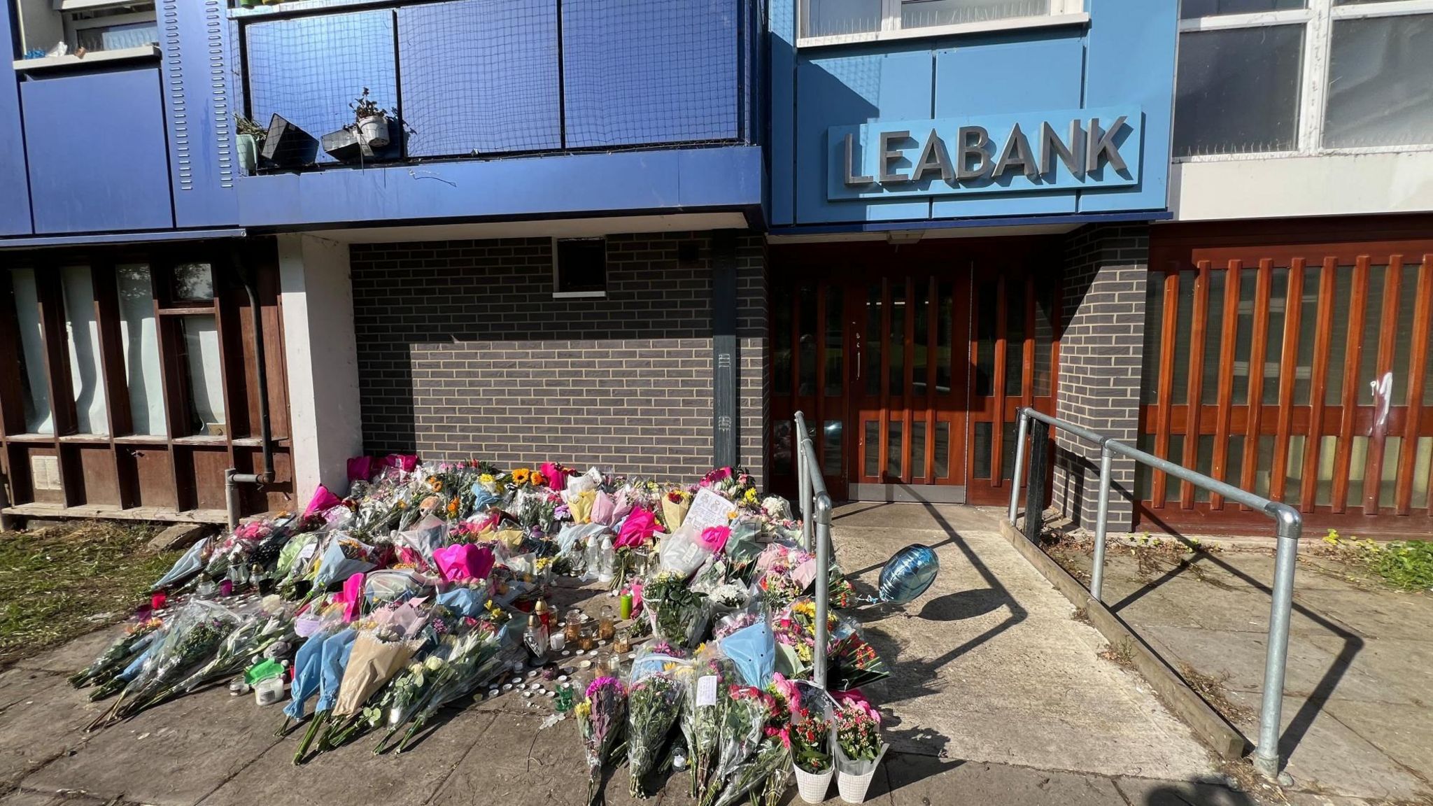 A large pile of flowers has been left outside the blue Leabank building near the access ramp to the building.