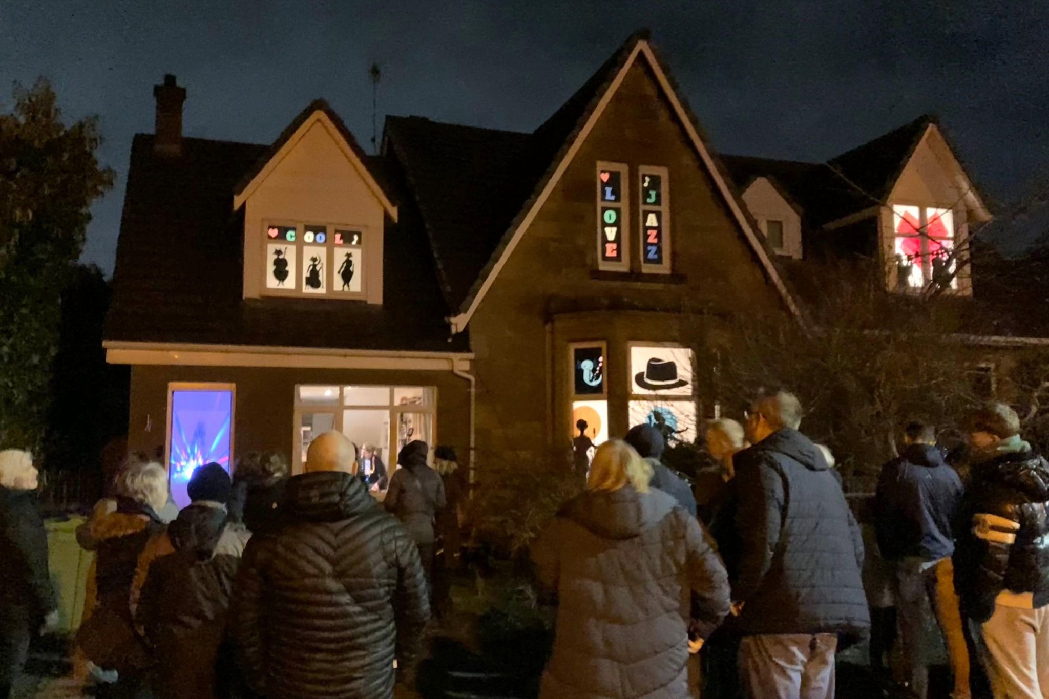 People crowd around a house with decorated windows