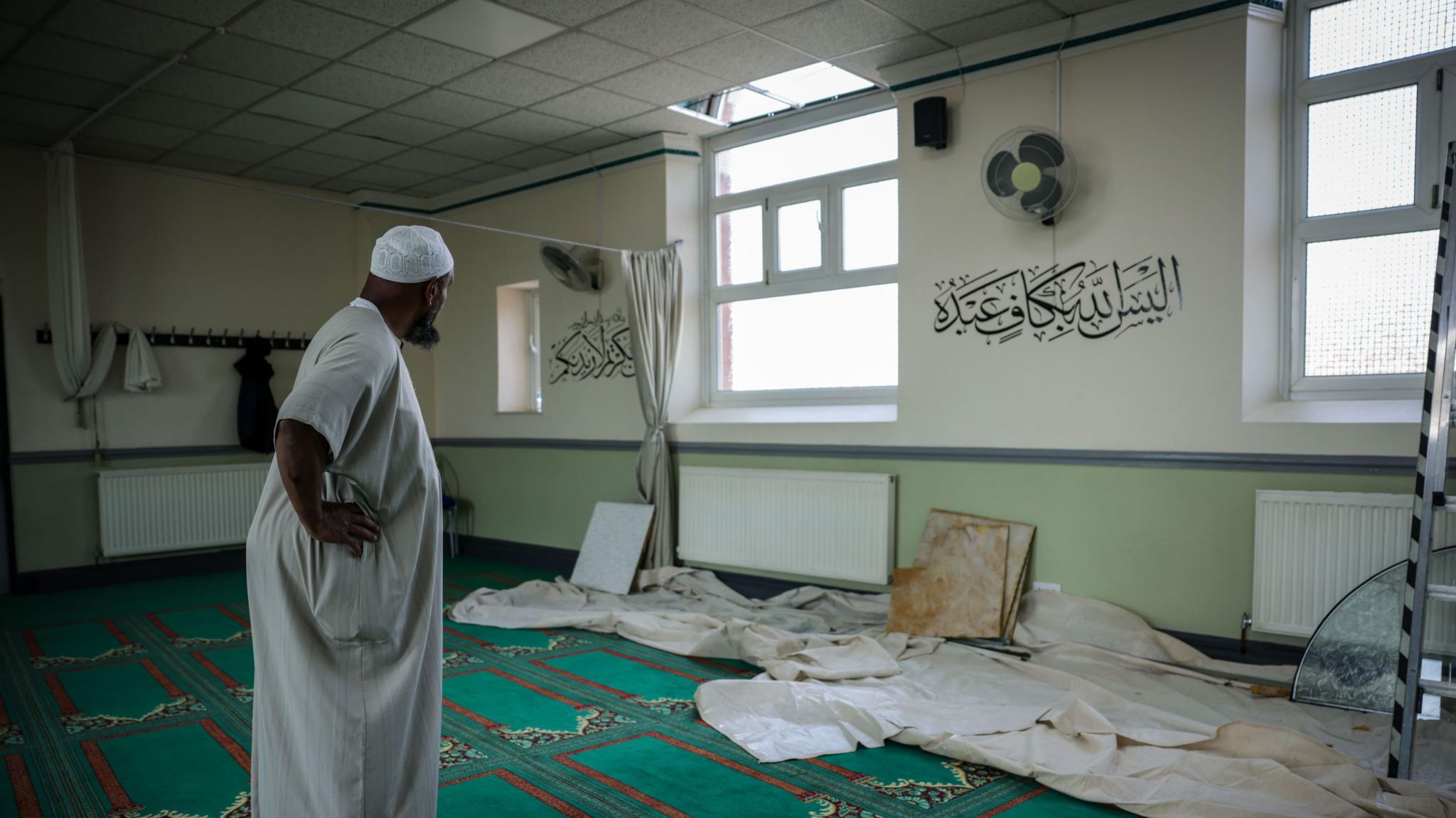 An imam at Southport Mosque, inspecting the damage inside, where missing windows and damaged ceiling tiles can be seen