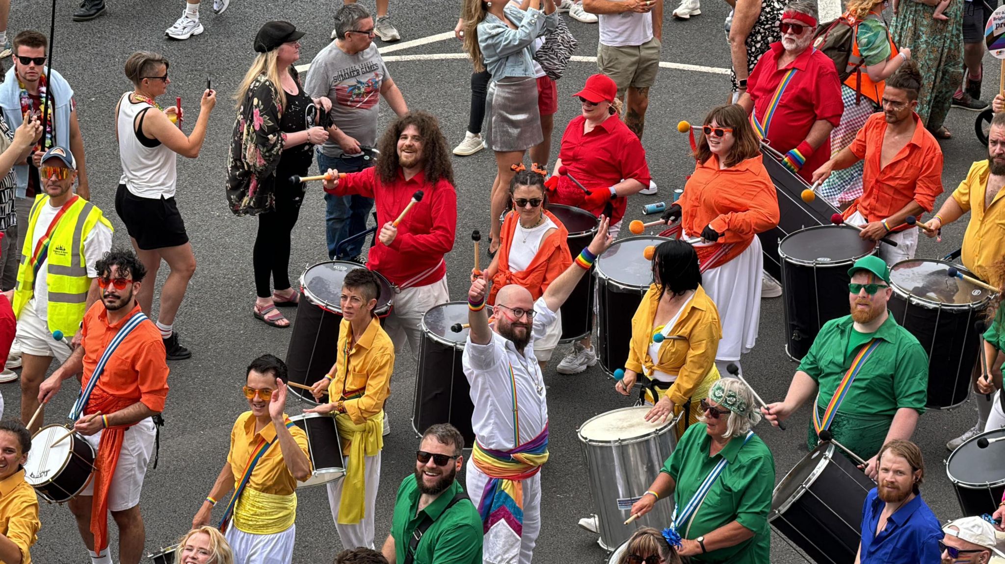 Drummers drumming in the street while wearing rainbow clothing