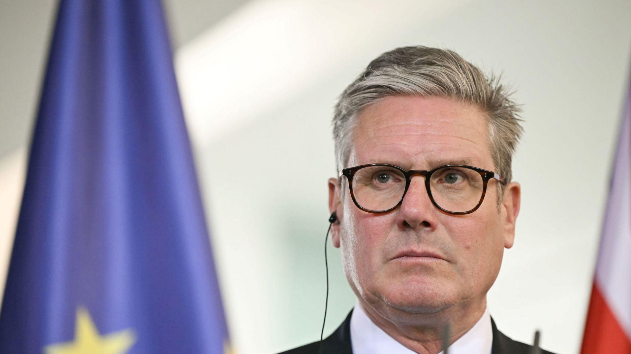 Sir Keir Starmer, frowning, with the flag of the European Union behind him