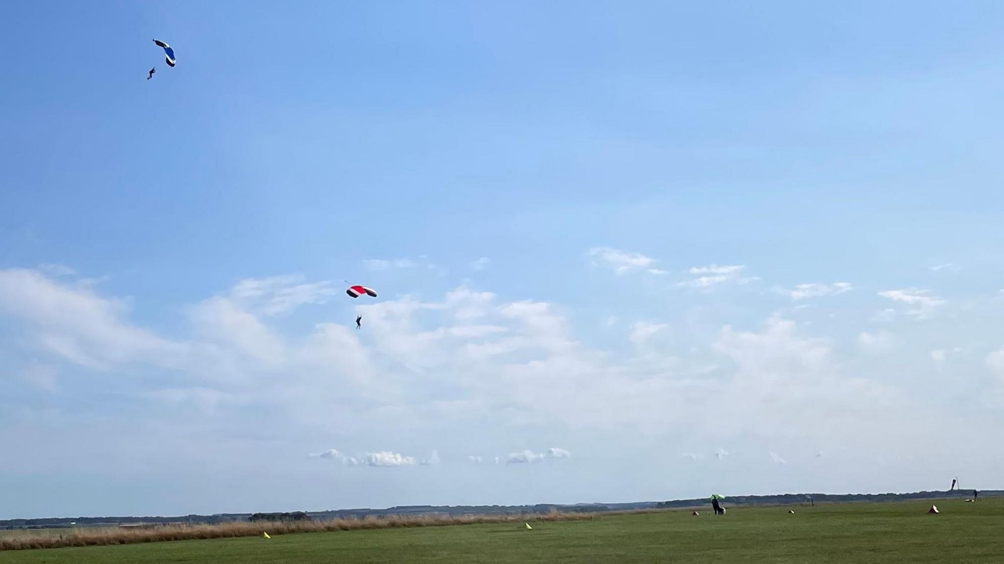 Field with blue sky showing skydivers parachuting down to the ground.